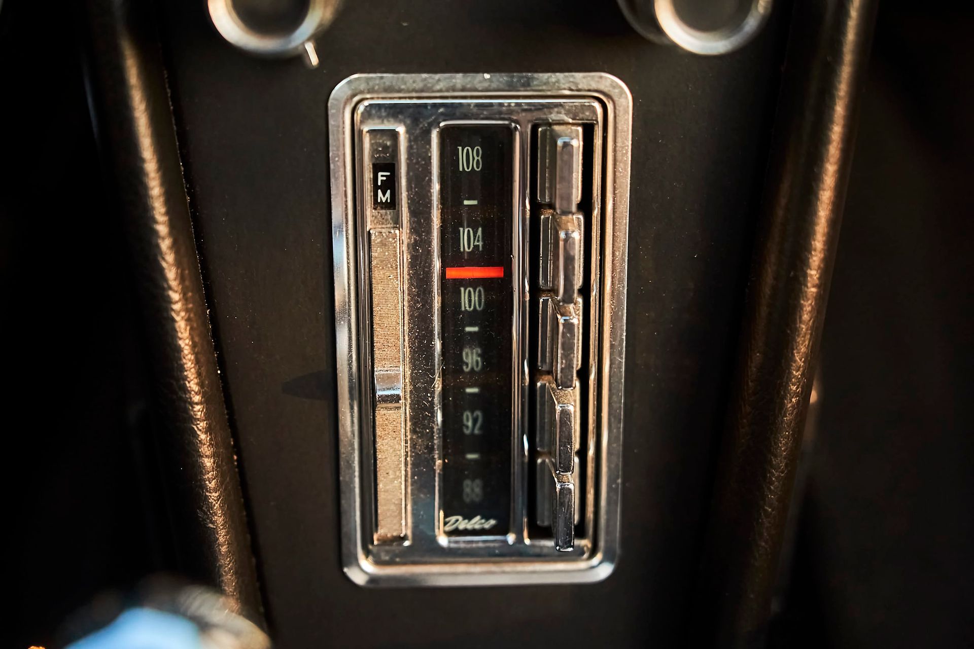 Close-up of a vintage car radio with a chrome bezel. The dial is set to 100 on the FM frequency.