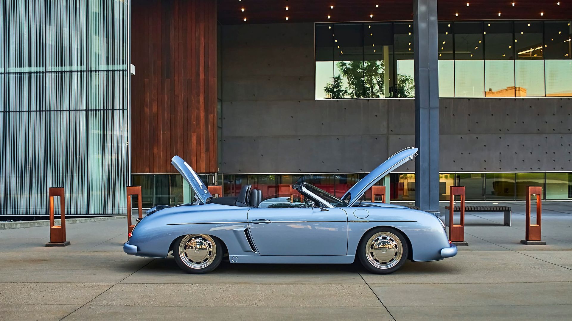 Light blue vintage car with open hood parked in front of a modern building.