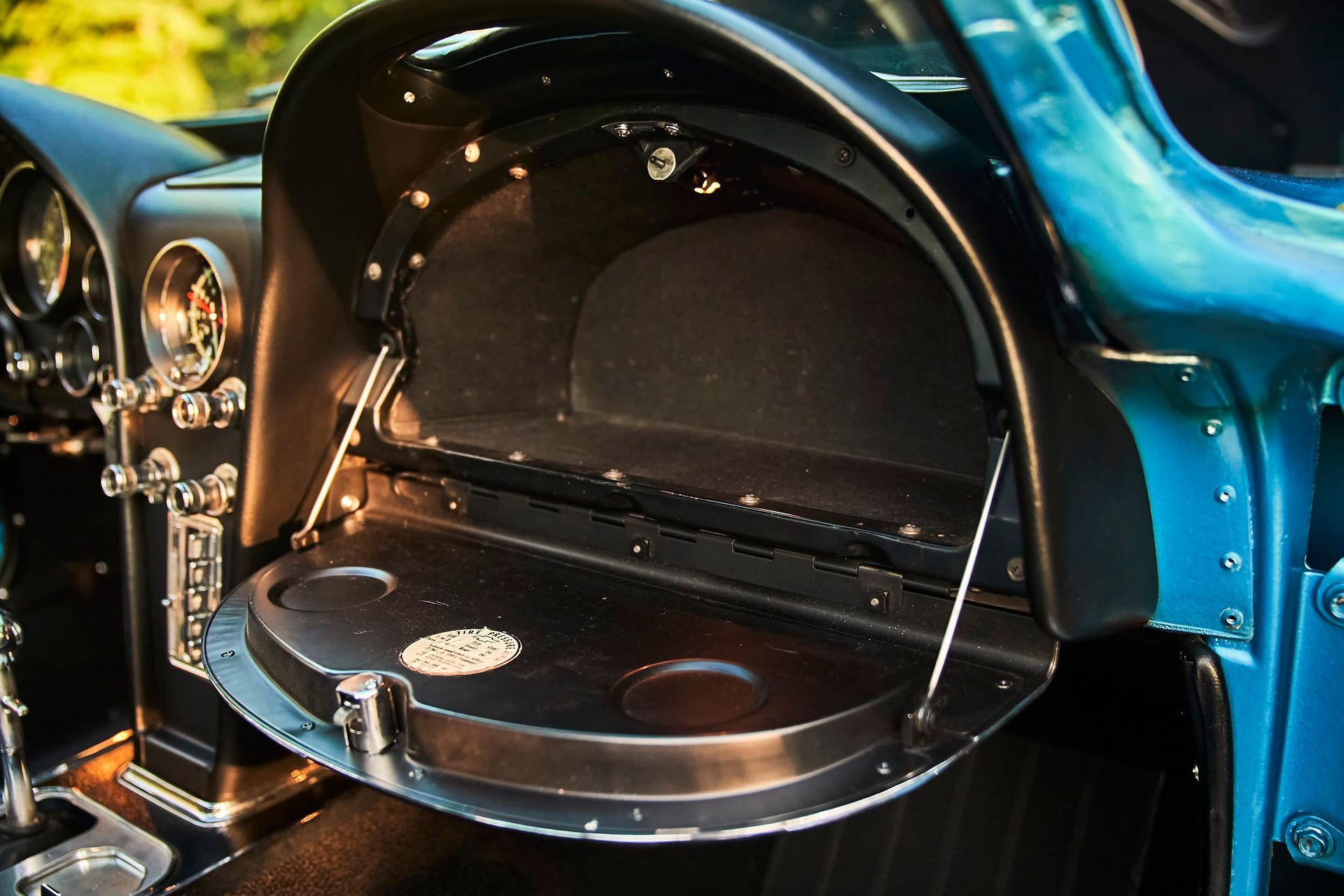 Open glove compartment with drink holders in a classic blue car's dashboard. Black interior with chrome accents.