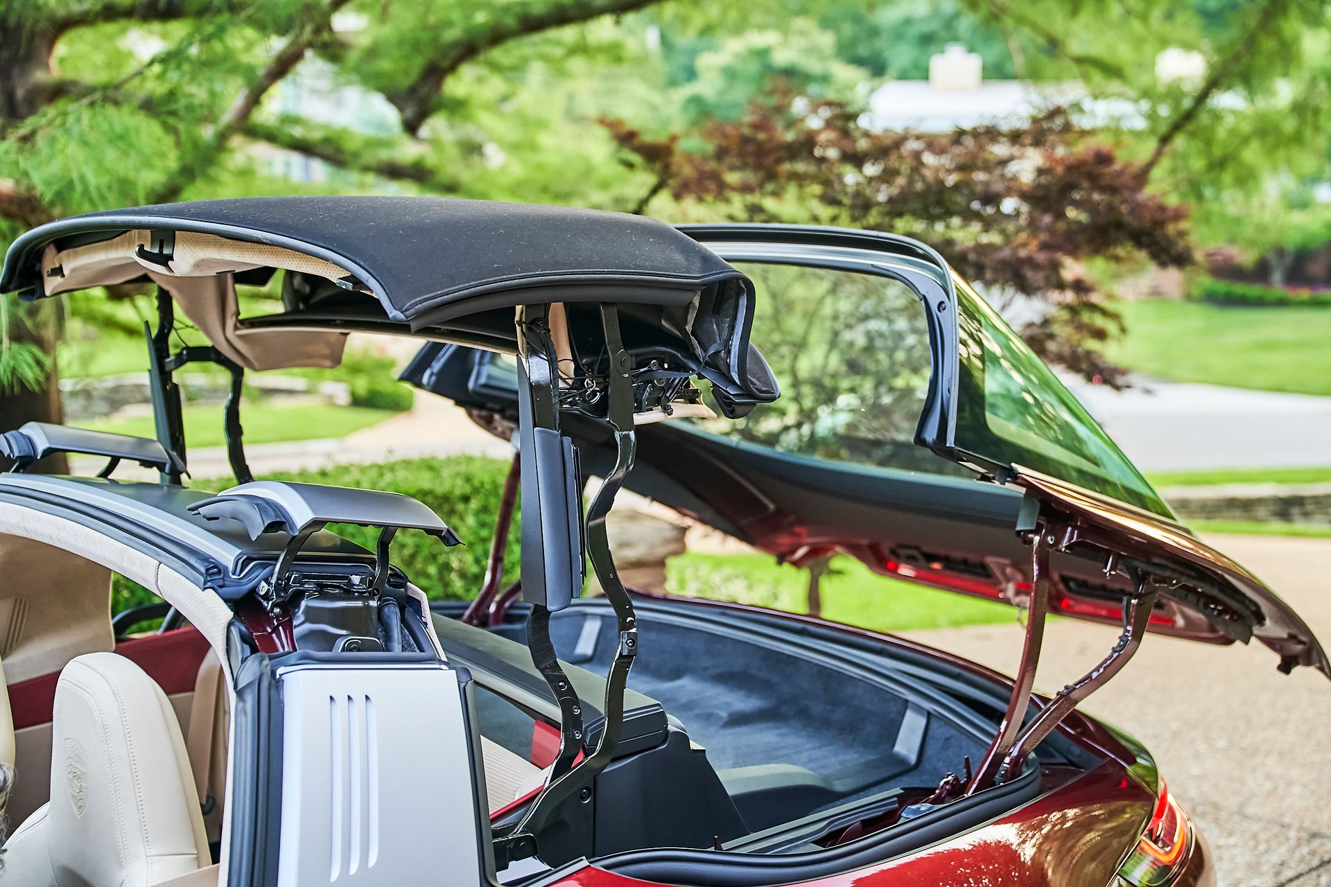A red convertible car with the hood open is parked in a driveway.