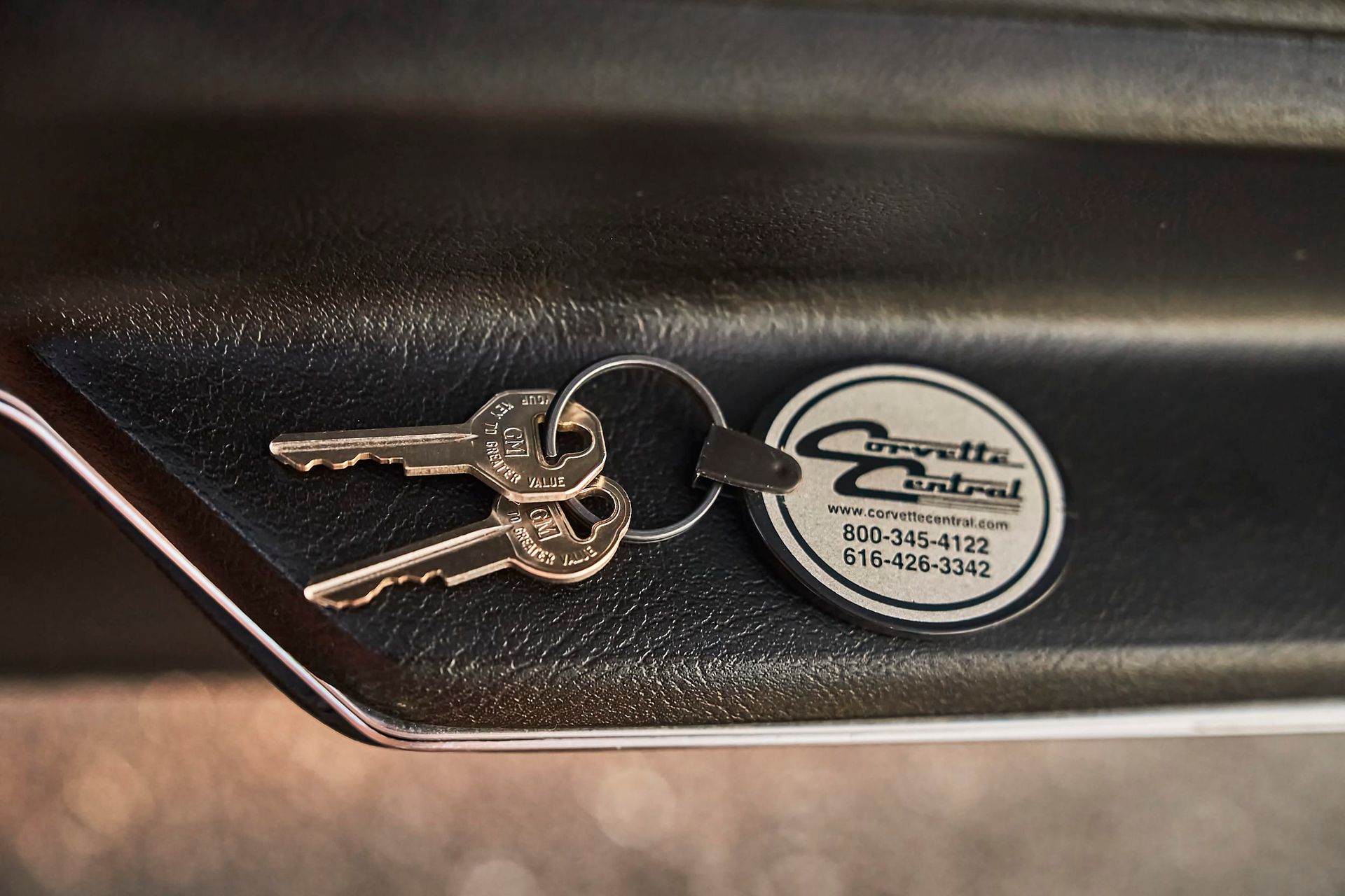 Two keys and a Corvette Central key fob on a black surface with chrome trim.