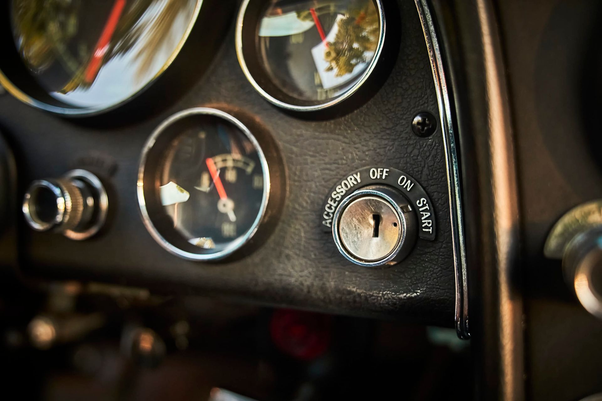 Close-up of a vintage car dashboard with the ignition key, gauges, and other controls. Black dashboard with chrome accents.