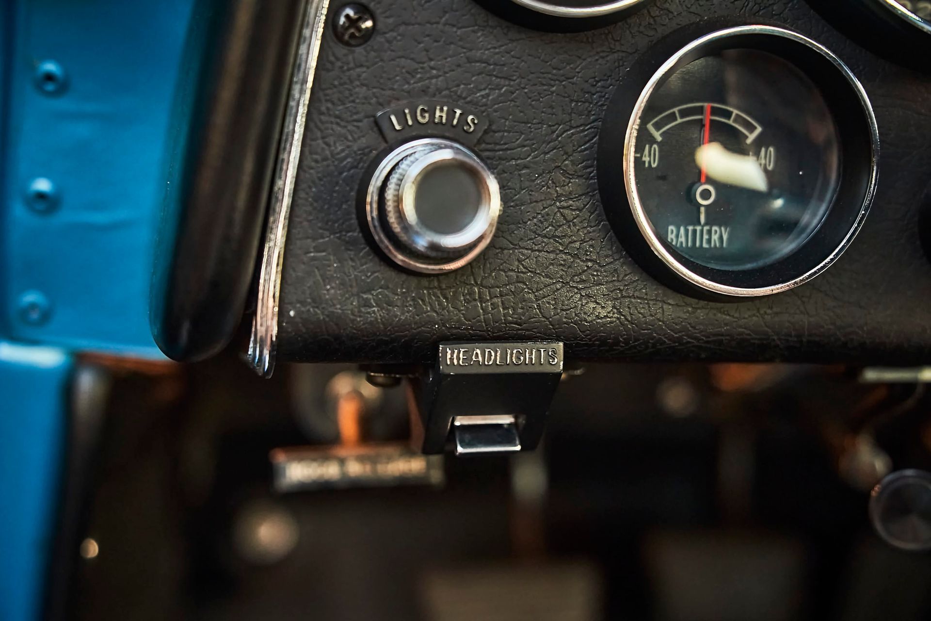 Close-up of a car's dashboard with a headlight switch, battery gauge, and fuel cut-off switch.