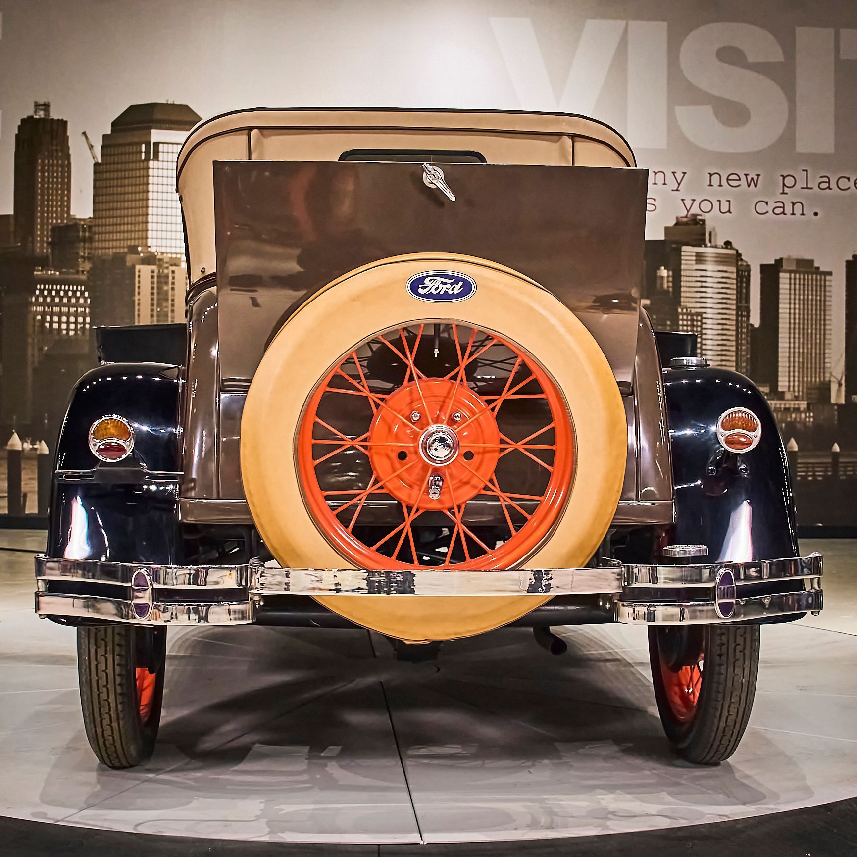An old ford car is on display in front of a city skyline