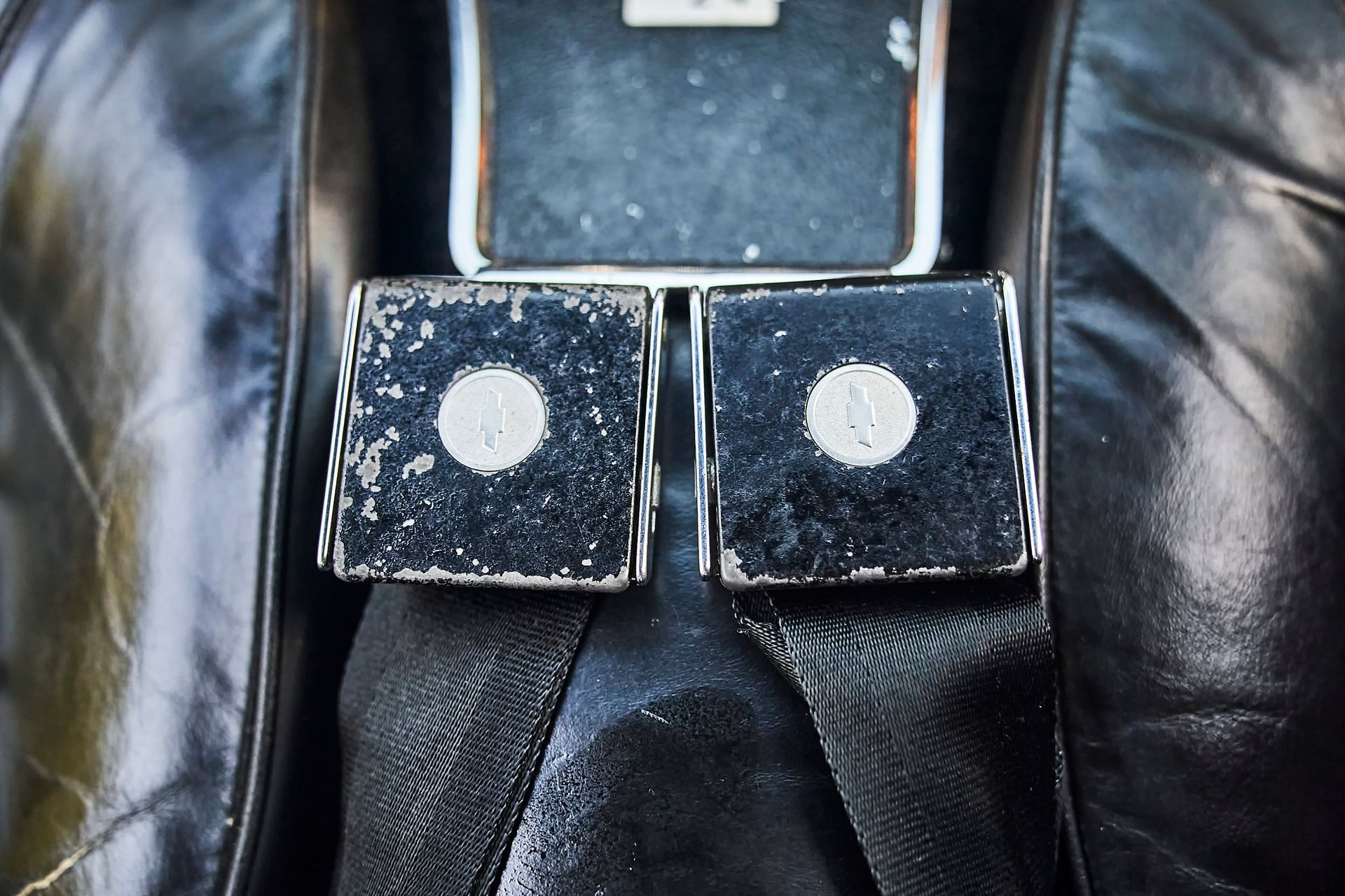 Two black, square cufflinks with white centers, set against a black leather garment.