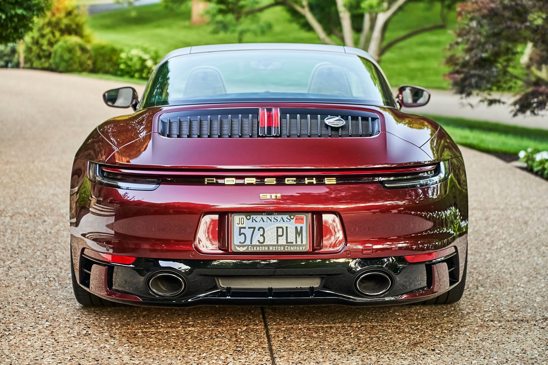 A red sports car is parked in a driveway with trees in the background.