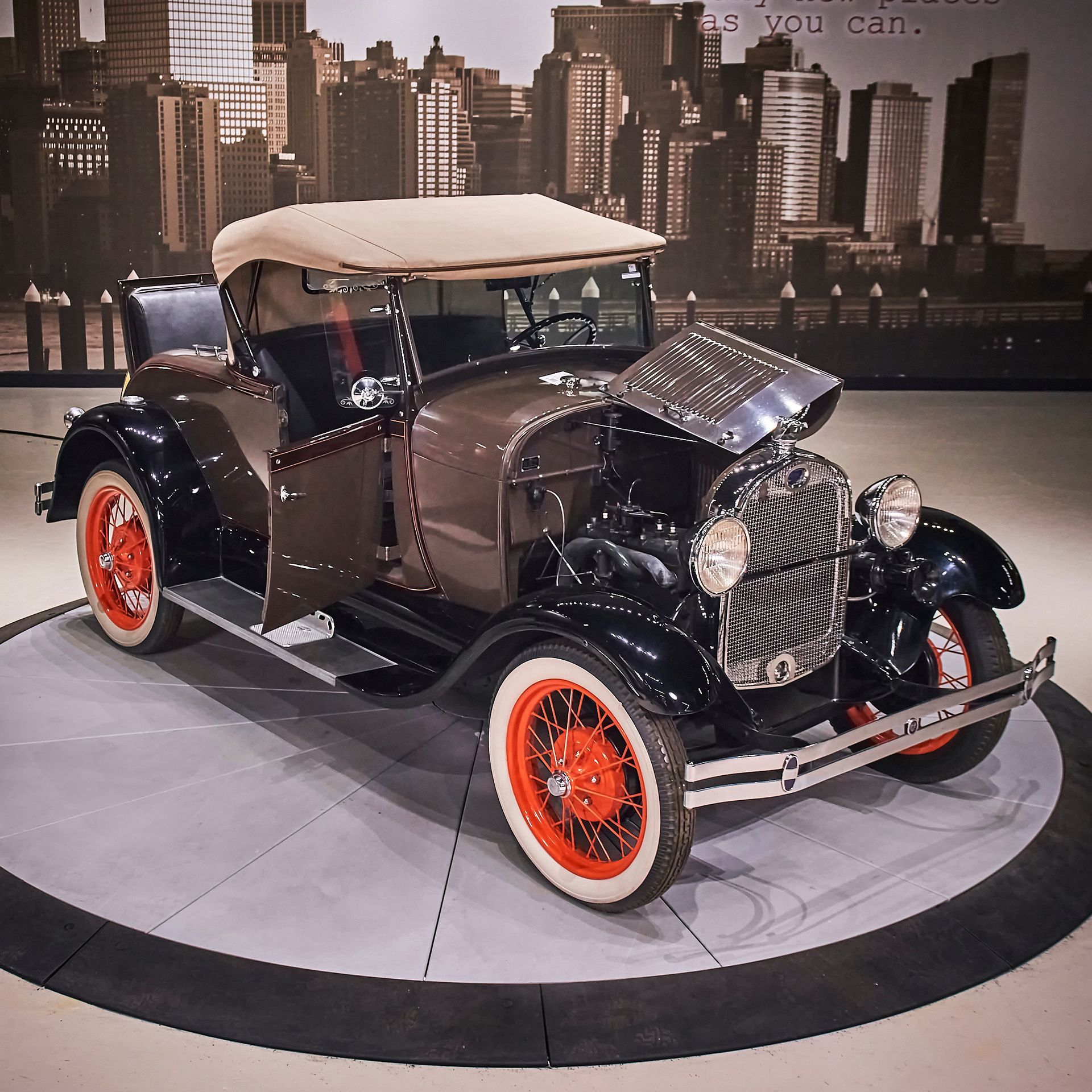 An old fashioned car is on display in front of a city skyline