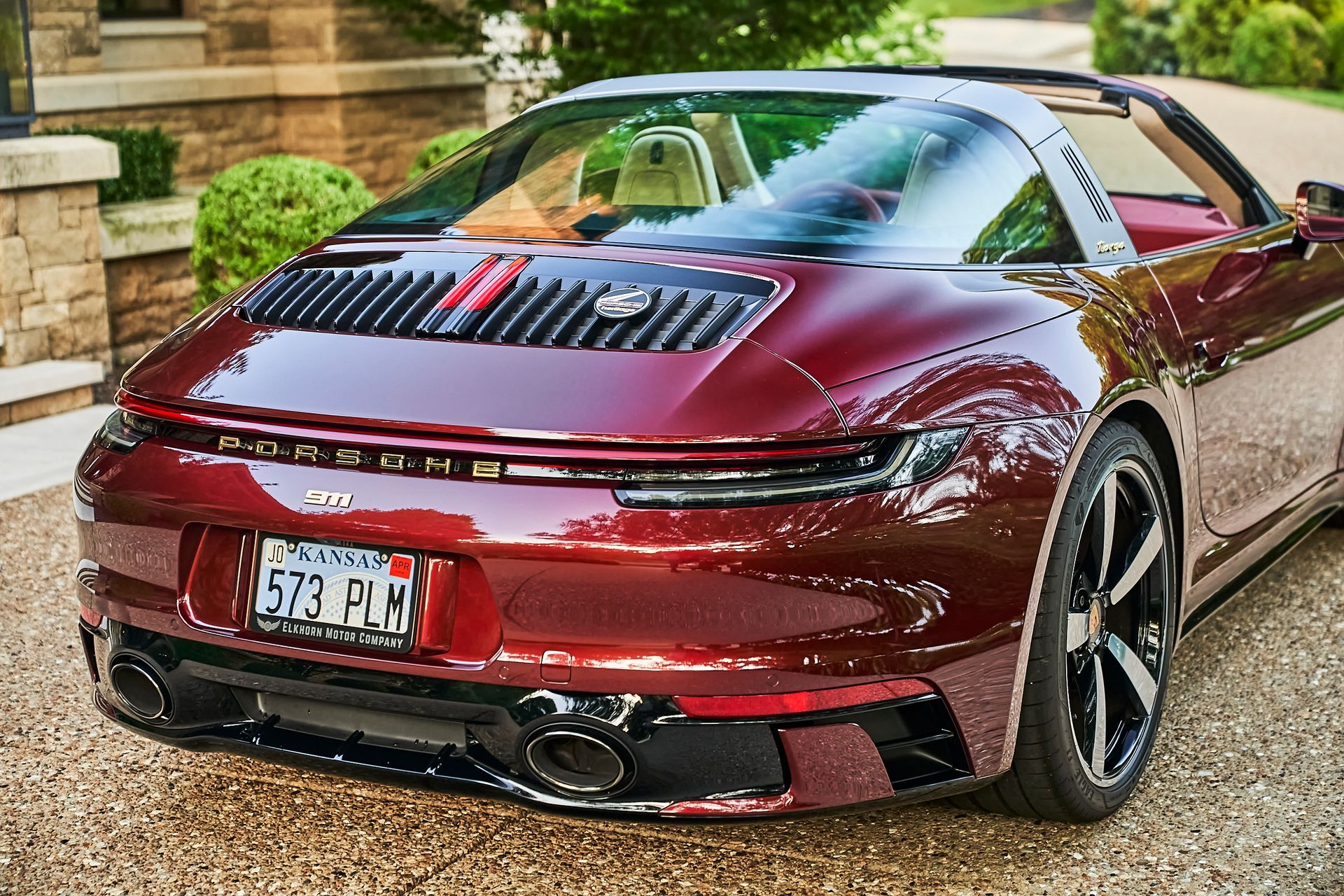 A red porsche targa is parked on a gravel driveway.