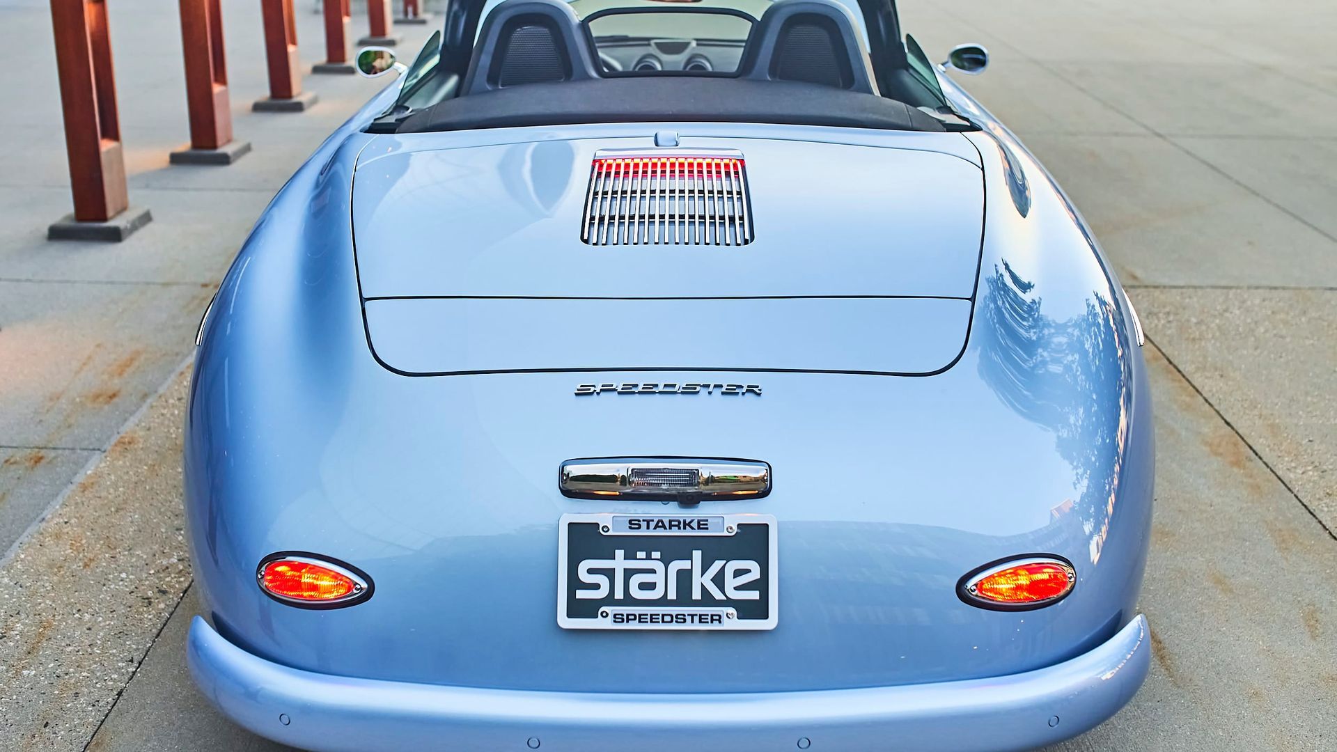 Light blue speedster car, rear view, parked with orange taillights and license plate.