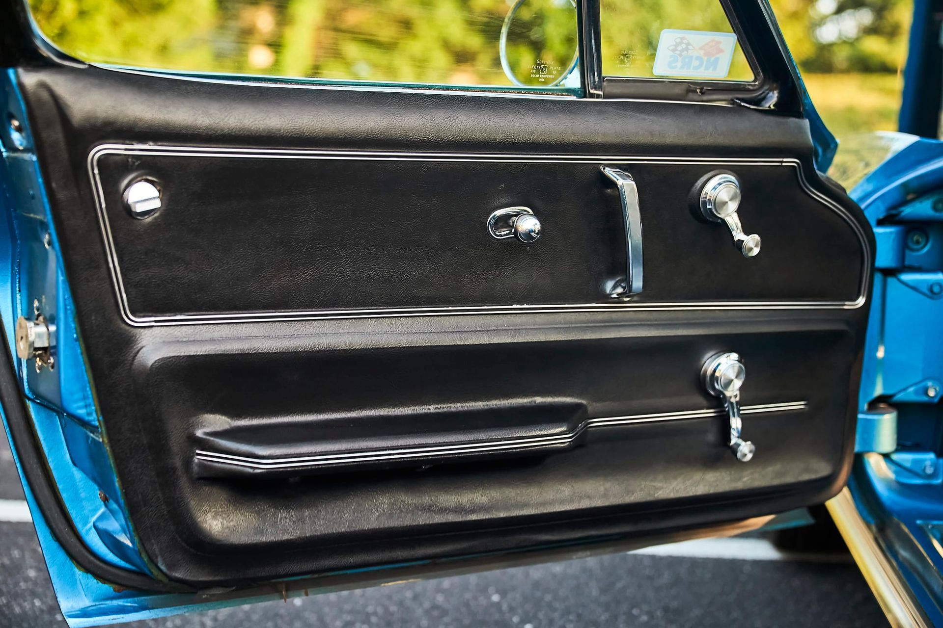 Black car door panel with chrome handles and trim, set in a blue car.