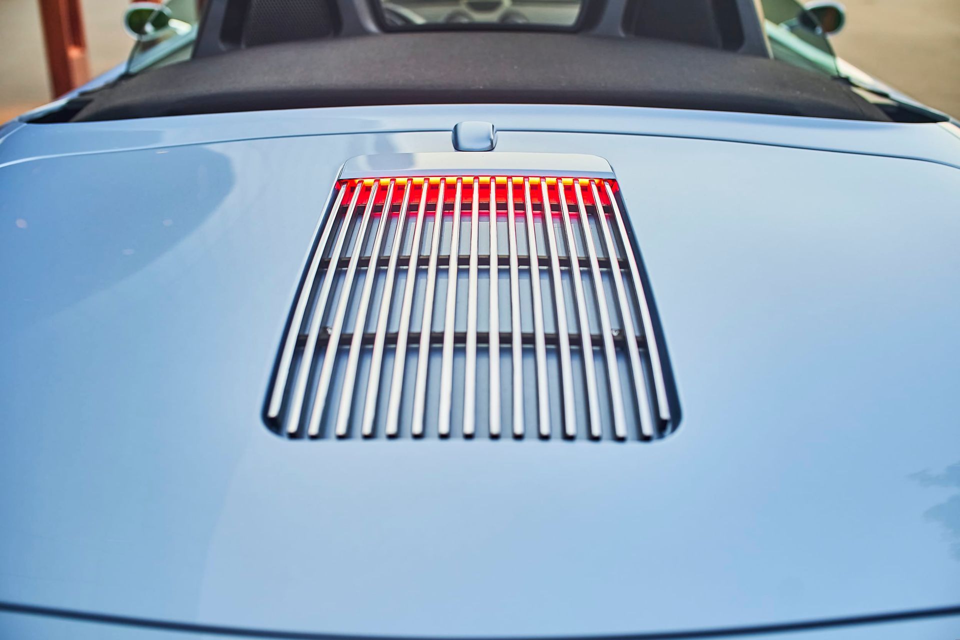 Light blue car's rear with a silver grill and red illuminated light.