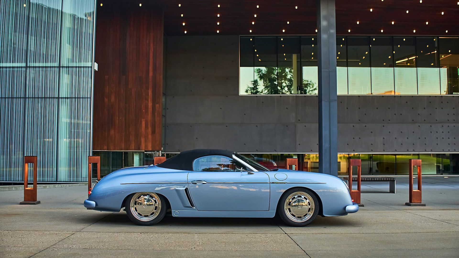 Light blue vintage convertible parked in front of a modern building with a dark wood facade.