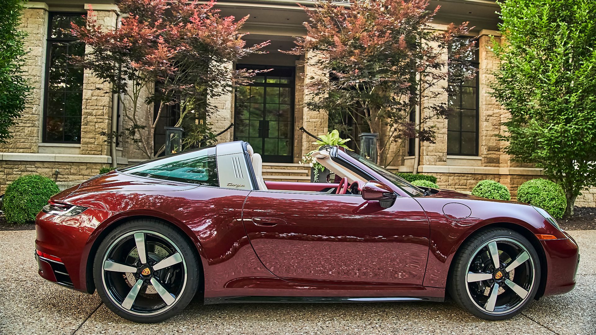 A red porsche targa is parked in front of a brick house.