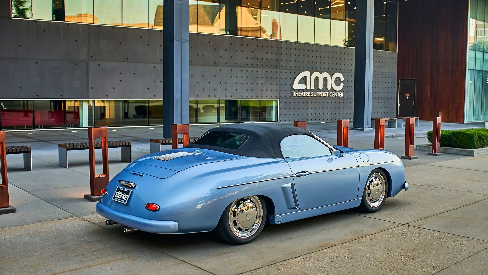 Light blue custom roadster parked in front of an AMC theater building. The convertible has a black top and chrome wheels.