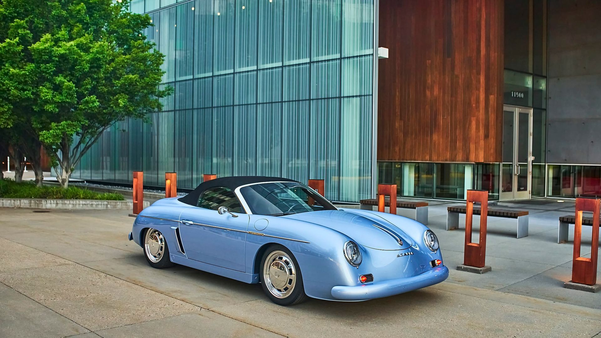 Light blue vintage Porsche convertible parked in front of a modern building with glass and wood panels.