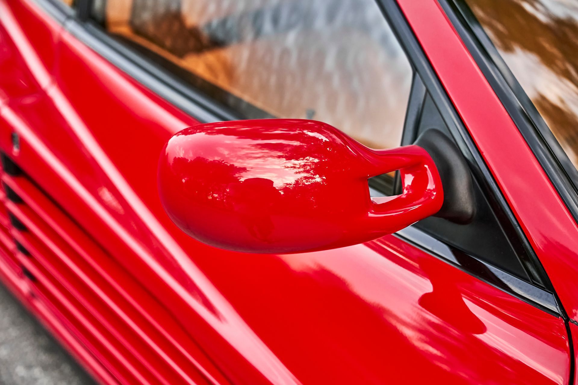 A close up of a red car 's side mirror.
