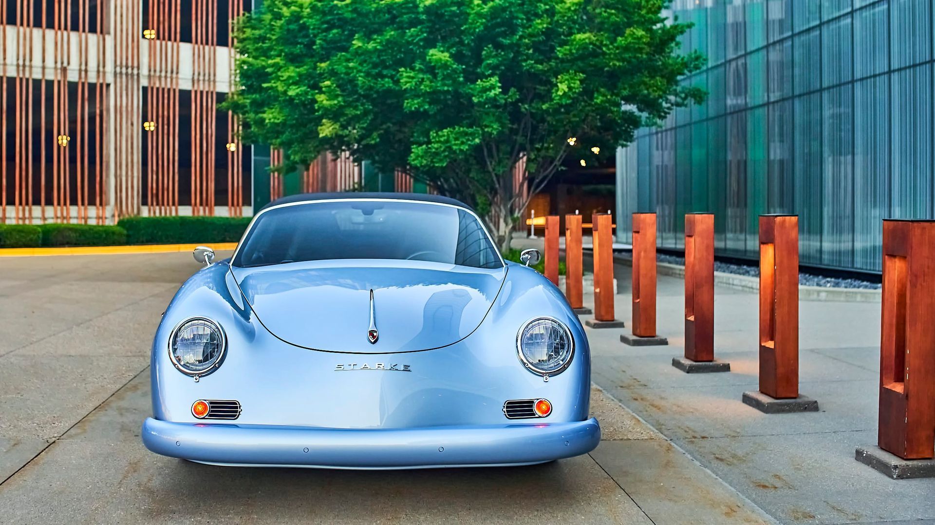 Light blue classic Porsche 356 parked outside a modern building with wooden light fixtures.