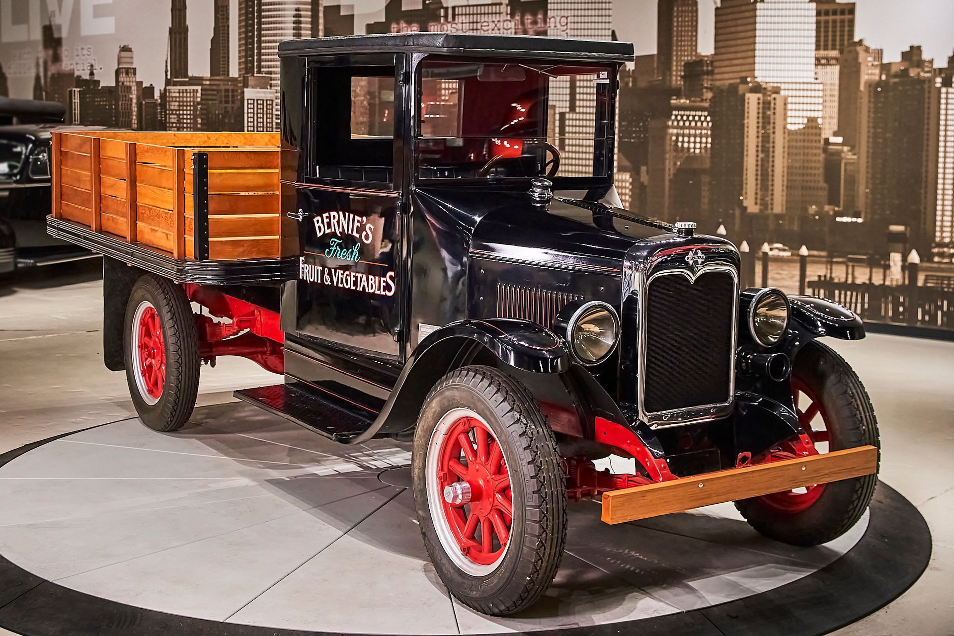 A black truck with a wooden bed is parked in front of a city skyline