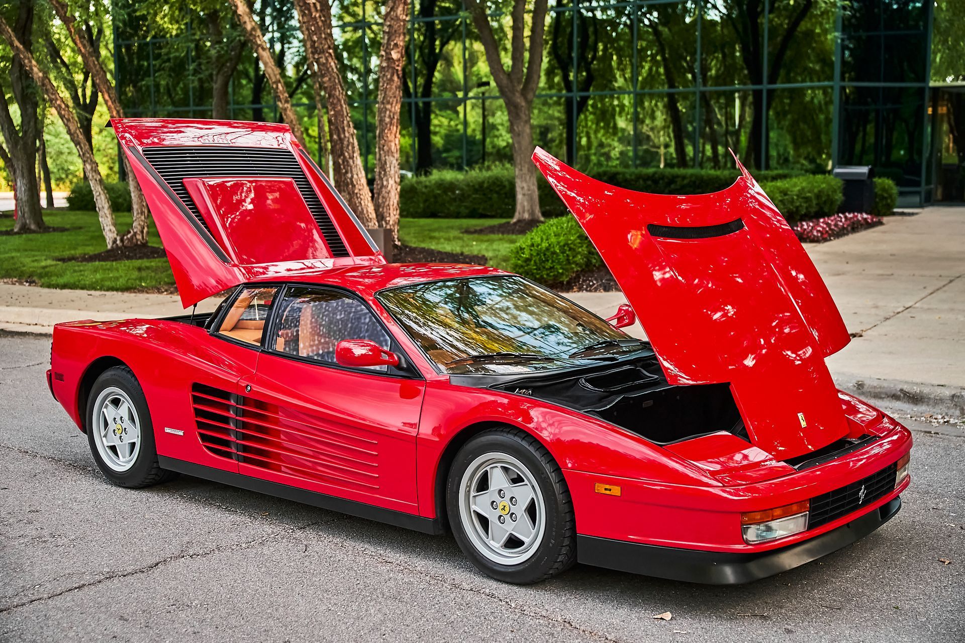 A red sports car with the hood up is parked on the side of the road.