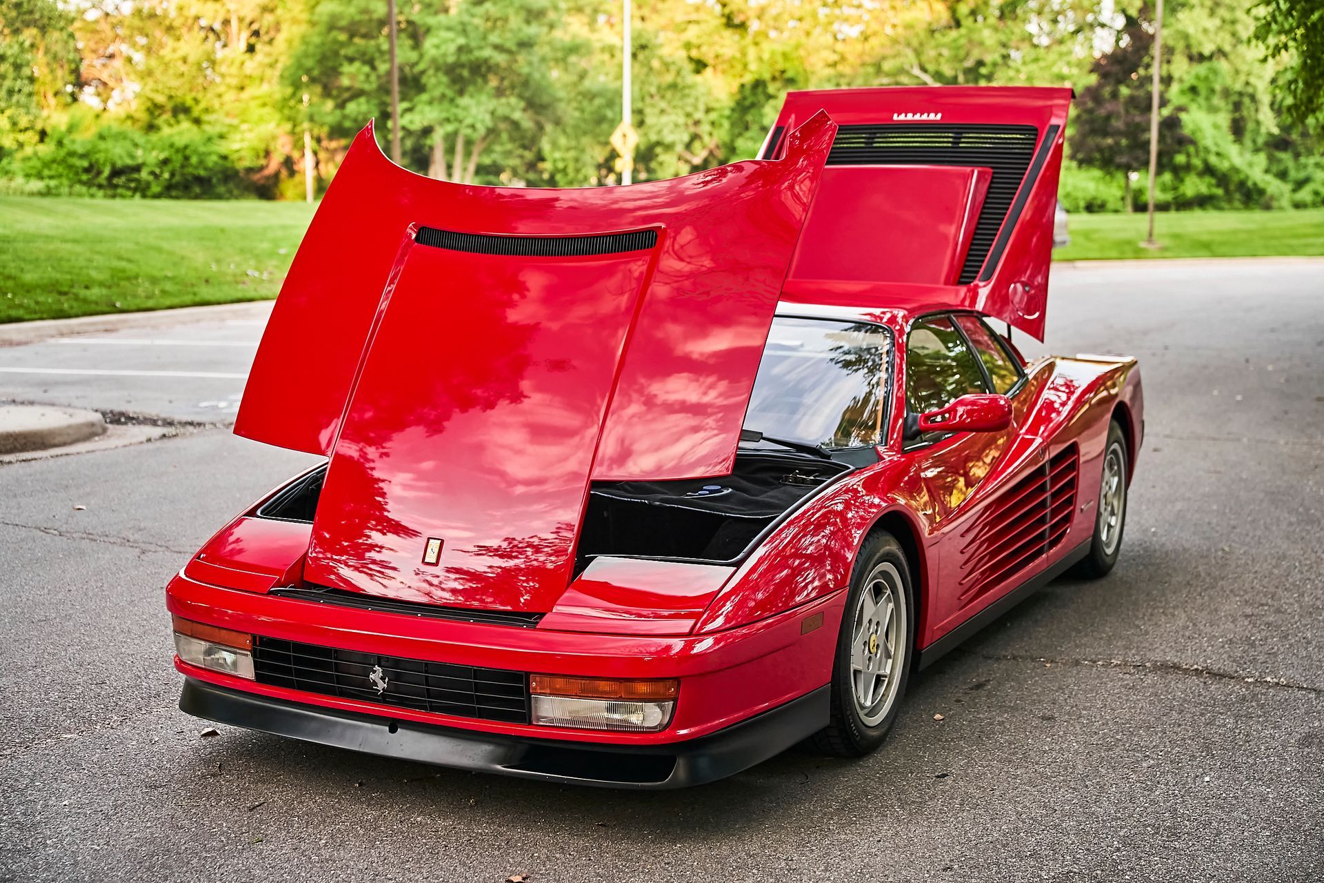 A red sports car with the hood up is parked on the side of the road.