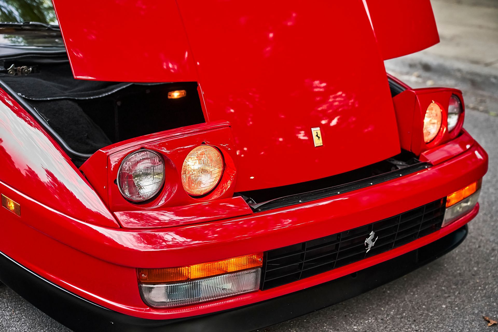 A red ferrari with the hood up is parked on the street.