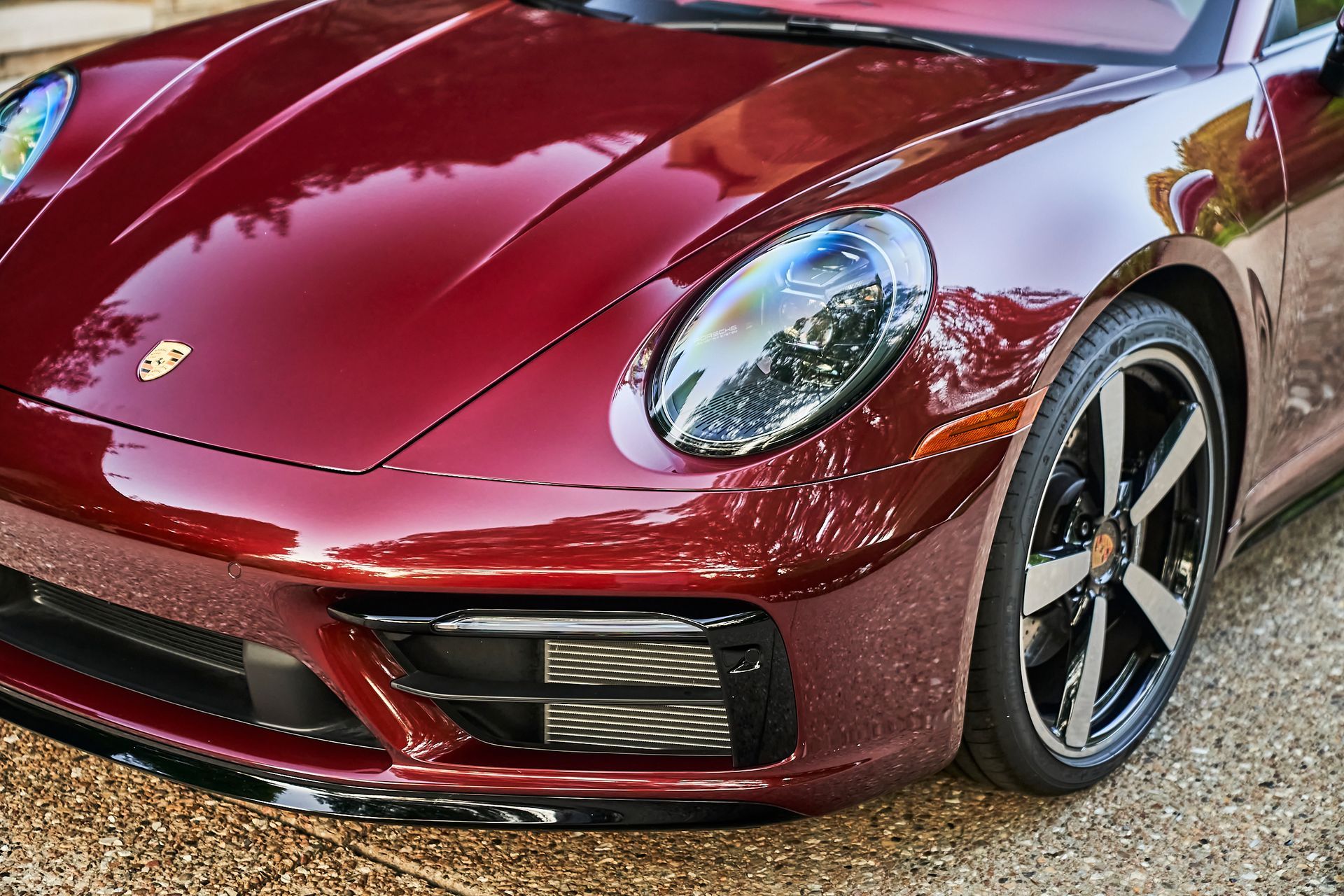 A red porsche 911 is parked on a gravel driveway.