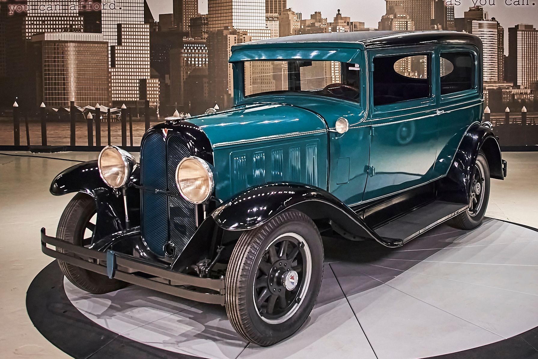 An old car is on display in front of a city skyline