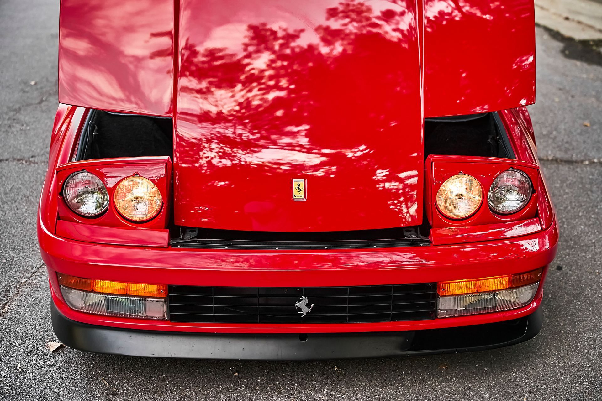 A red ferrari with the hood up is parked on the street.