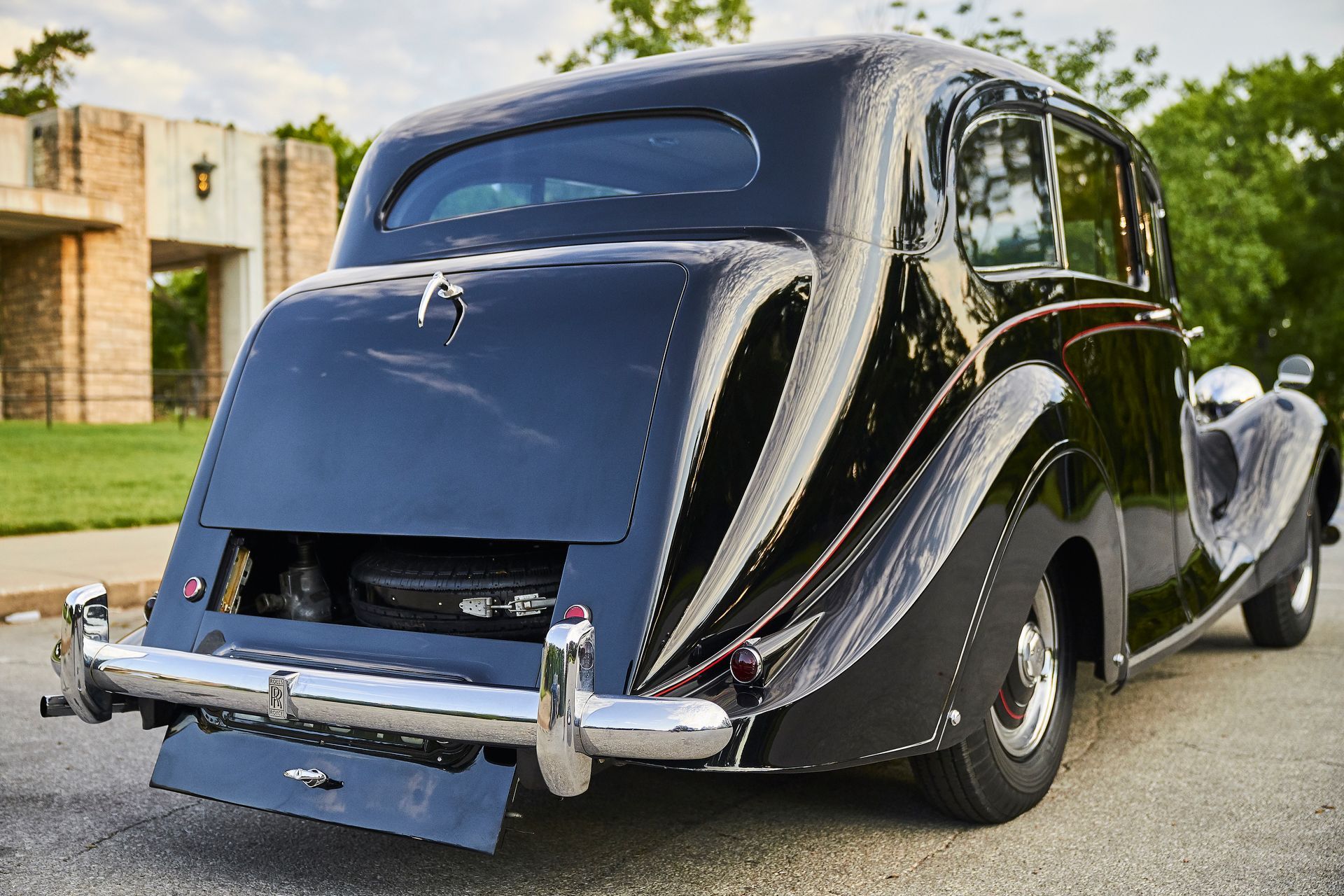 A black car with a suitcase in the back is parked on the side of the road.