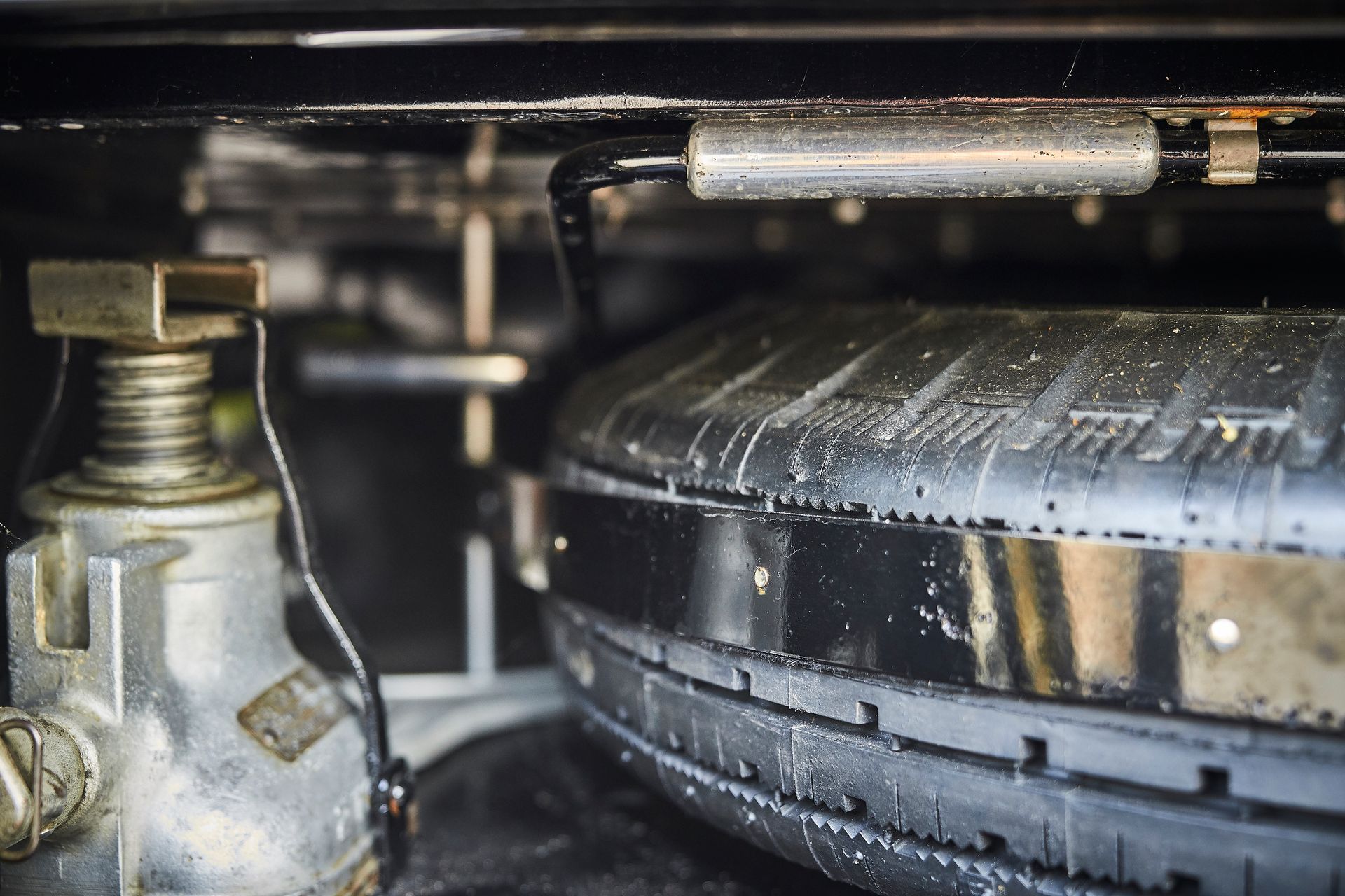 A tire is sitting under a jack in a car.