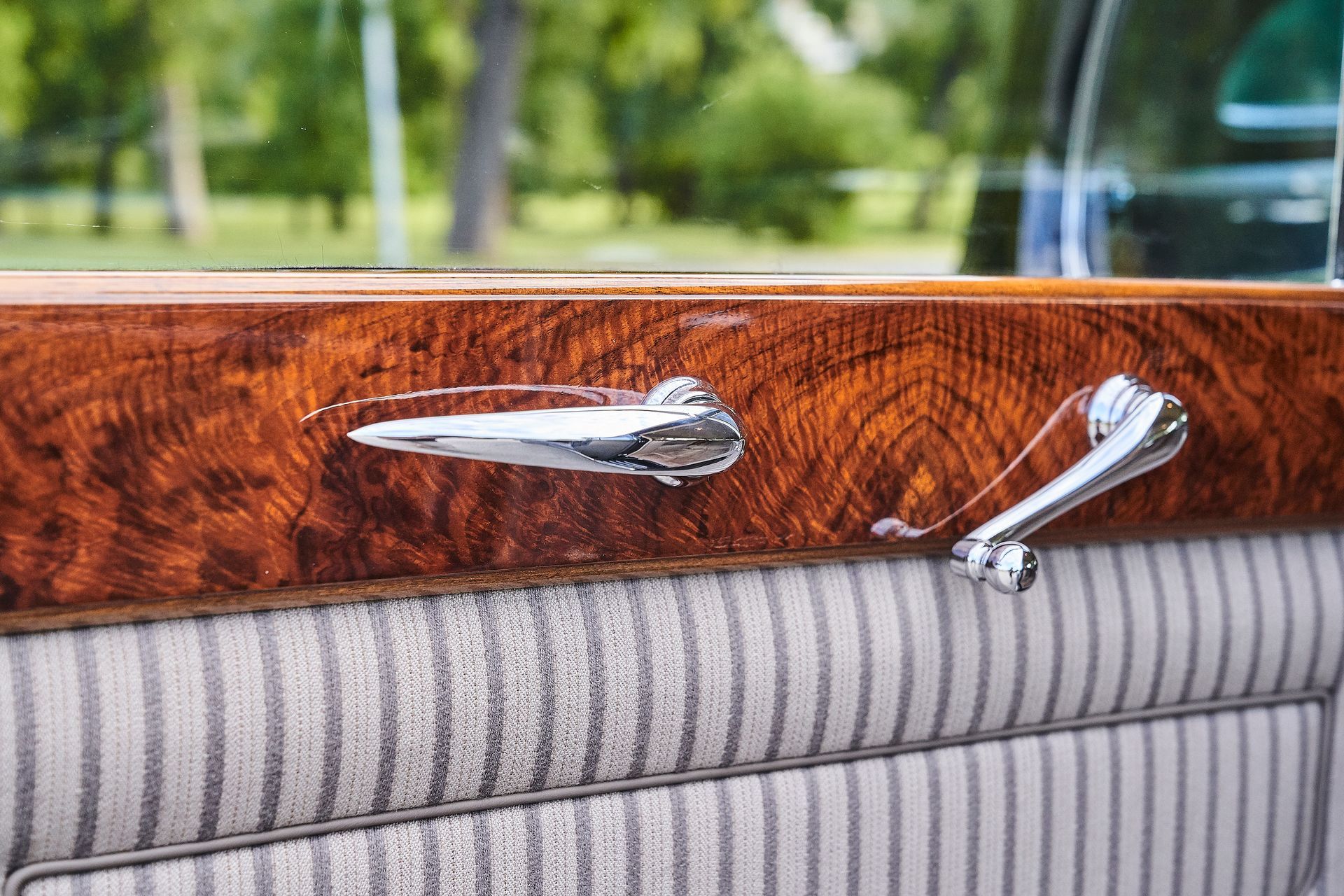 A close up of a car door with a wooden trim and a chrome handle.