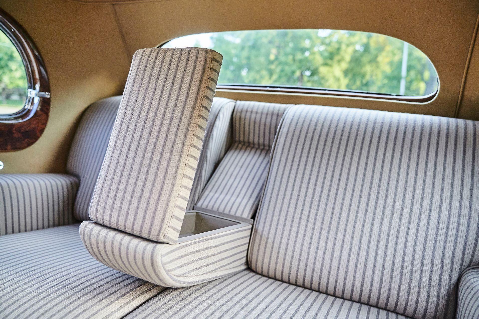 The back seat of a car with a striped couch and a window.