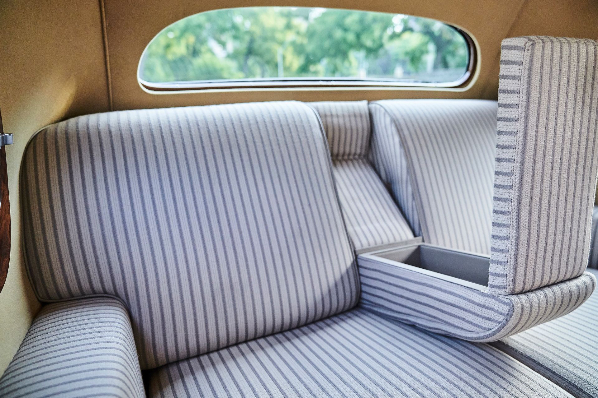 The back seat of a car with a striped couch and a window.