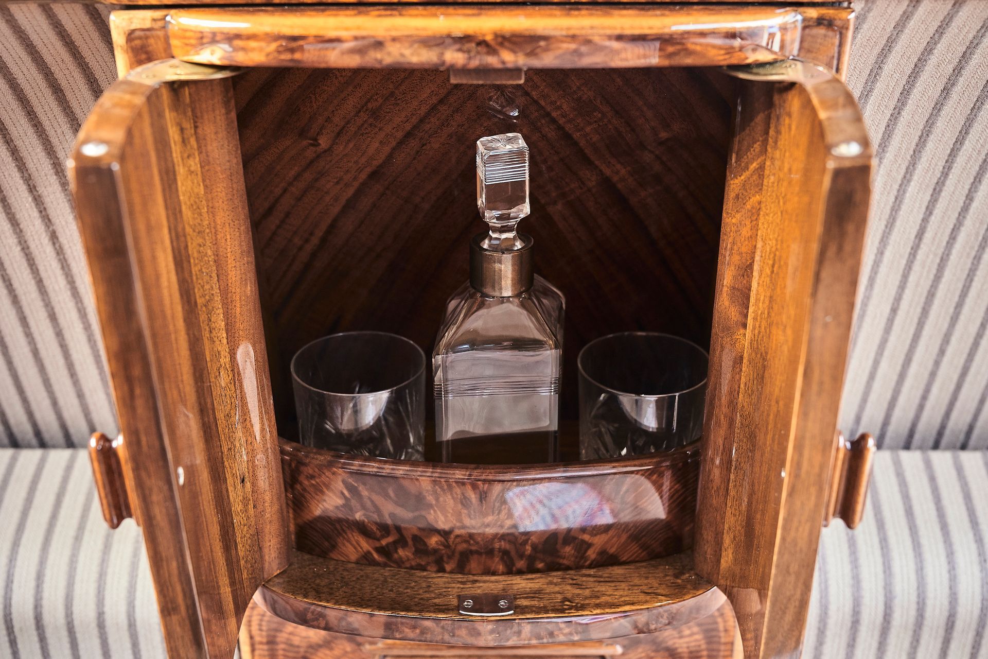 A wooden cabinet with a bottle of alcohol and two glasses inside of it.