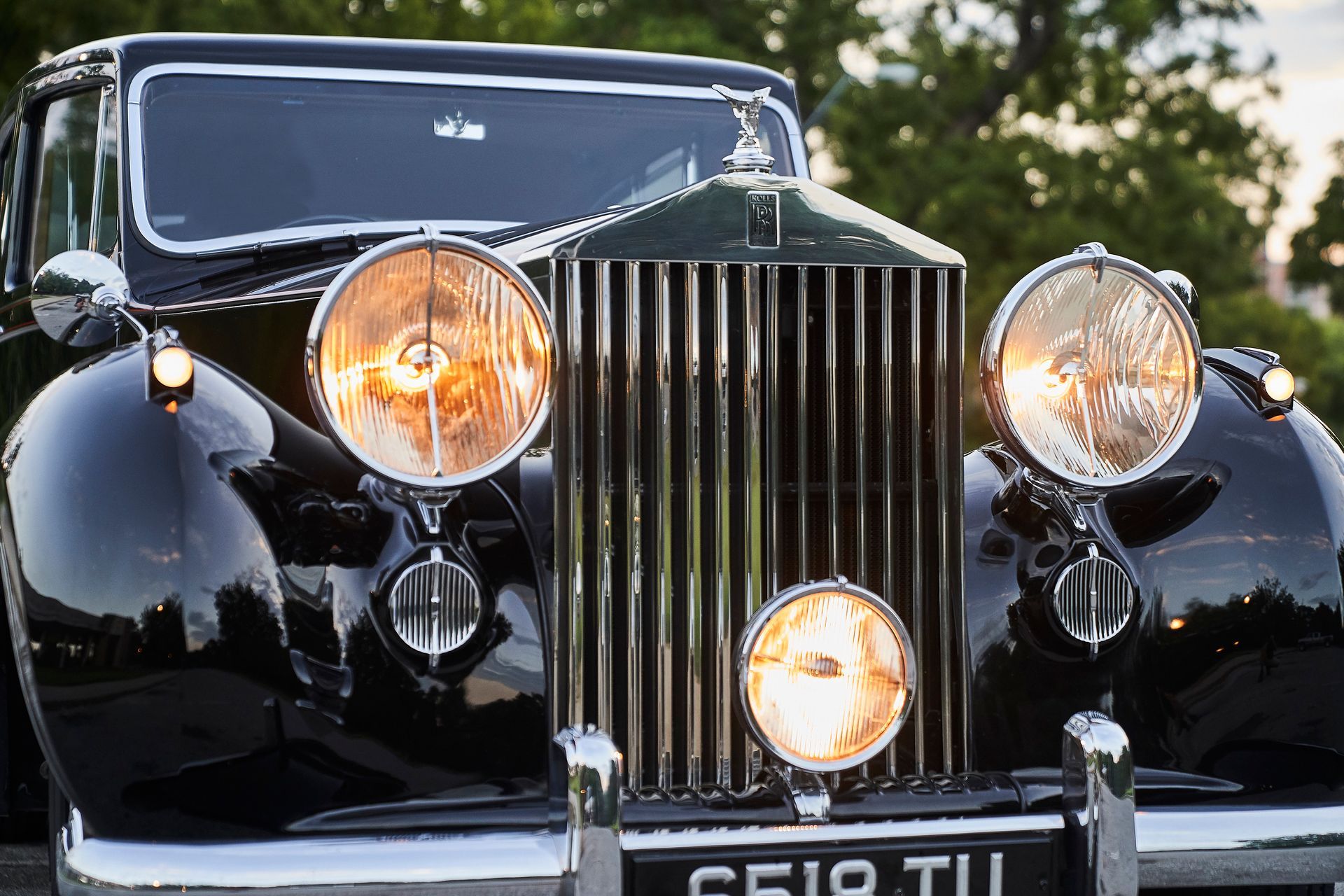 A black rolls royce car is parked in front of trees.