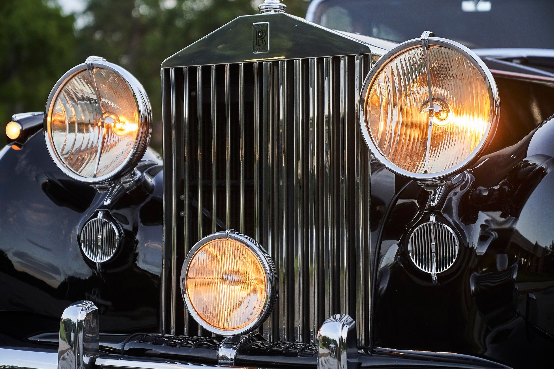The front of a black rolls royce car with the lights on.
