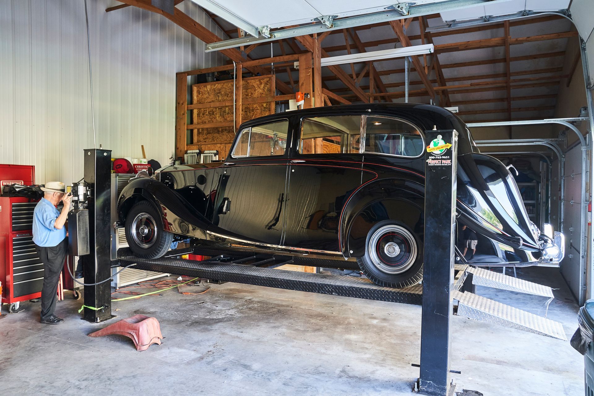 A man is standing next to a car on a lift in a garage.