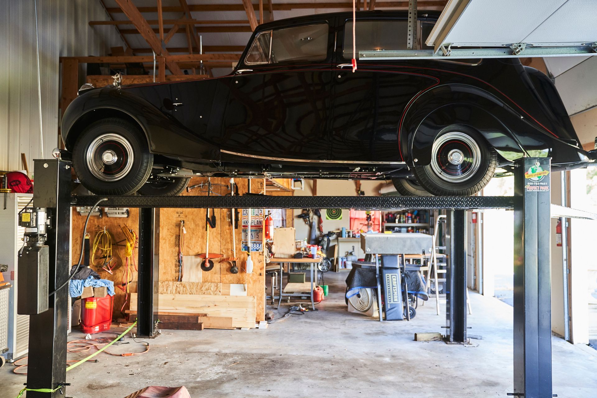 A black car is sitting on a lift in a garage.