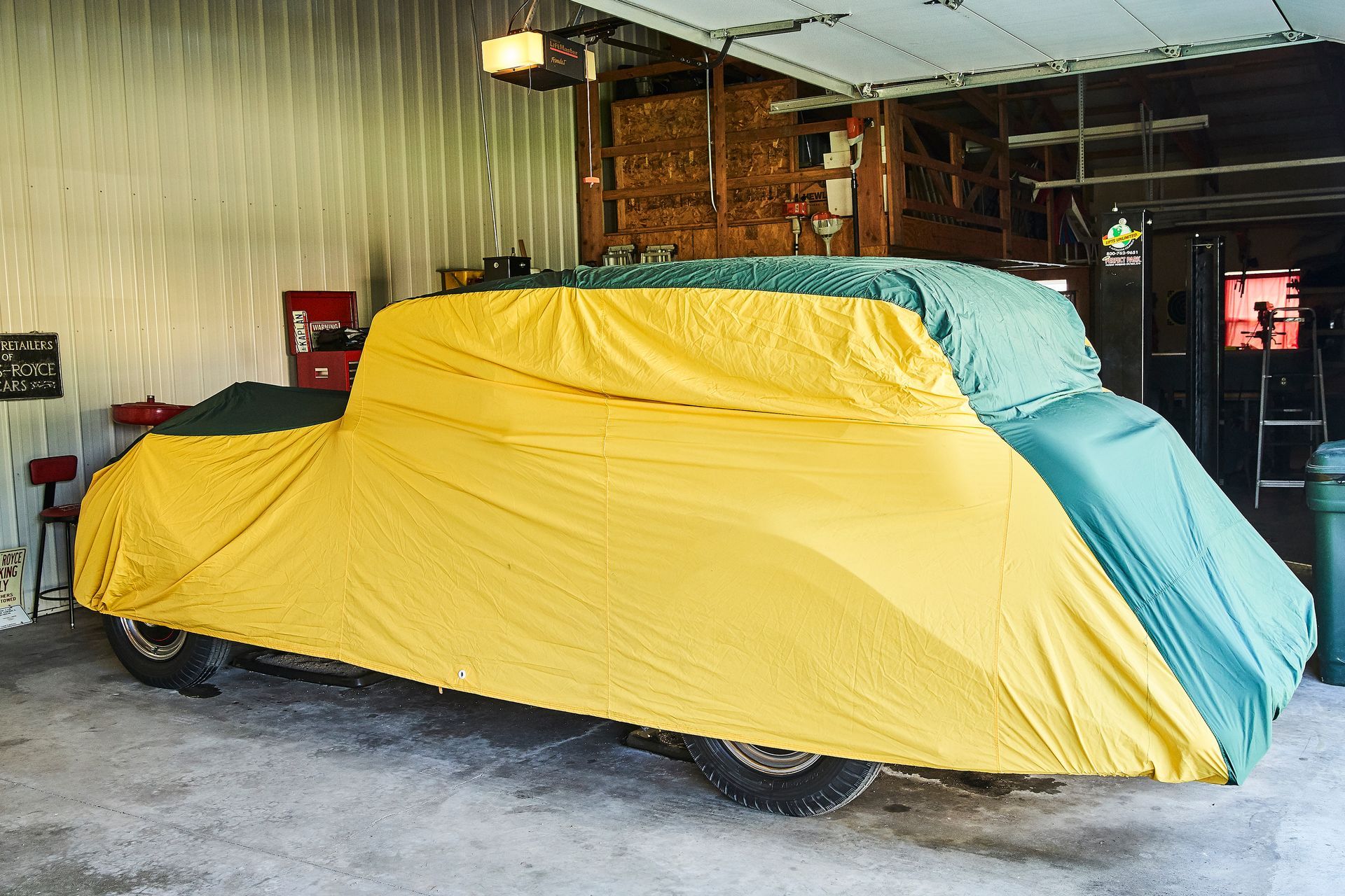 A car is covered in a yellow and green cover in a garage