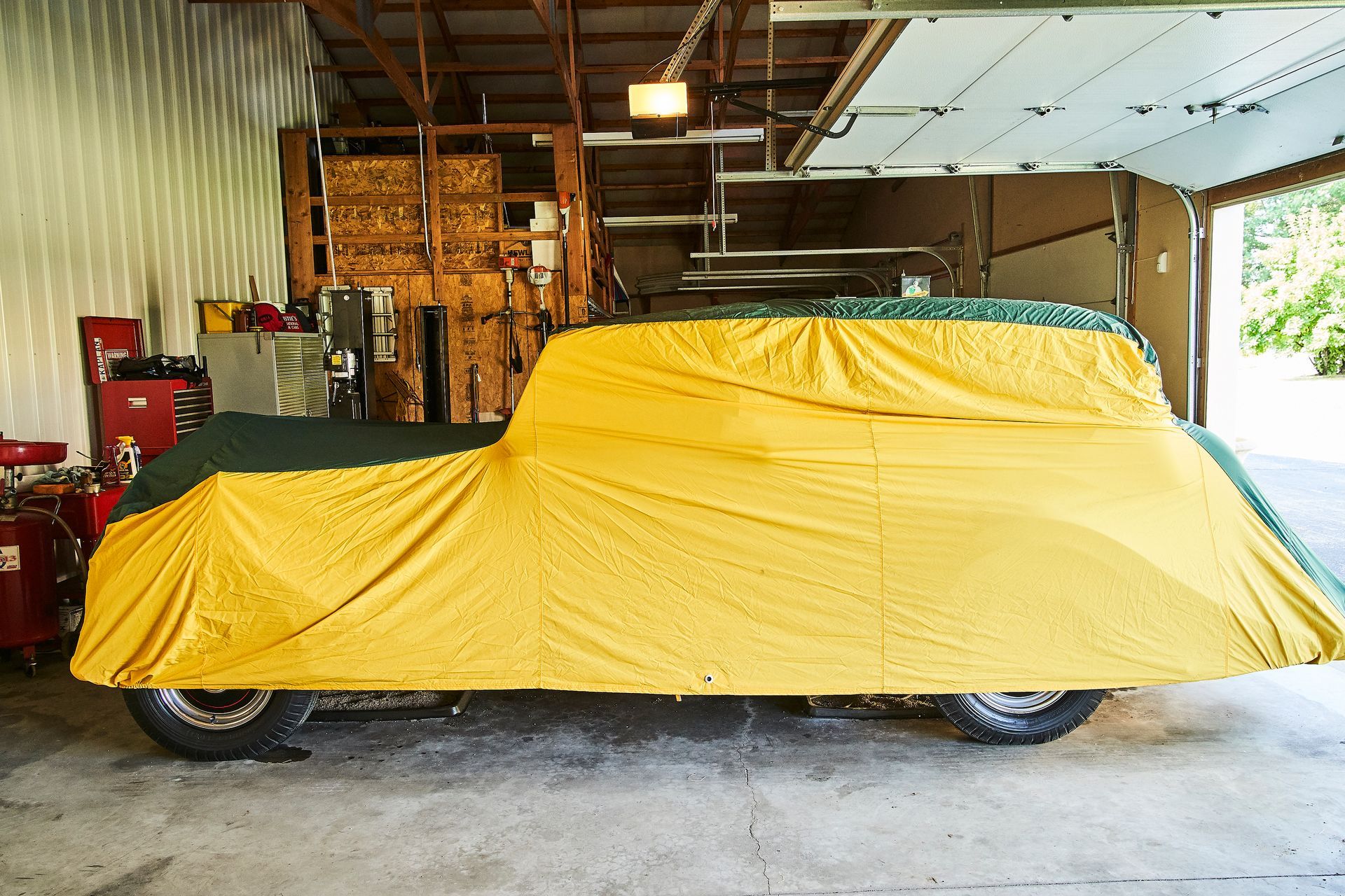 A car is covered in a yellow tarp in a garage.