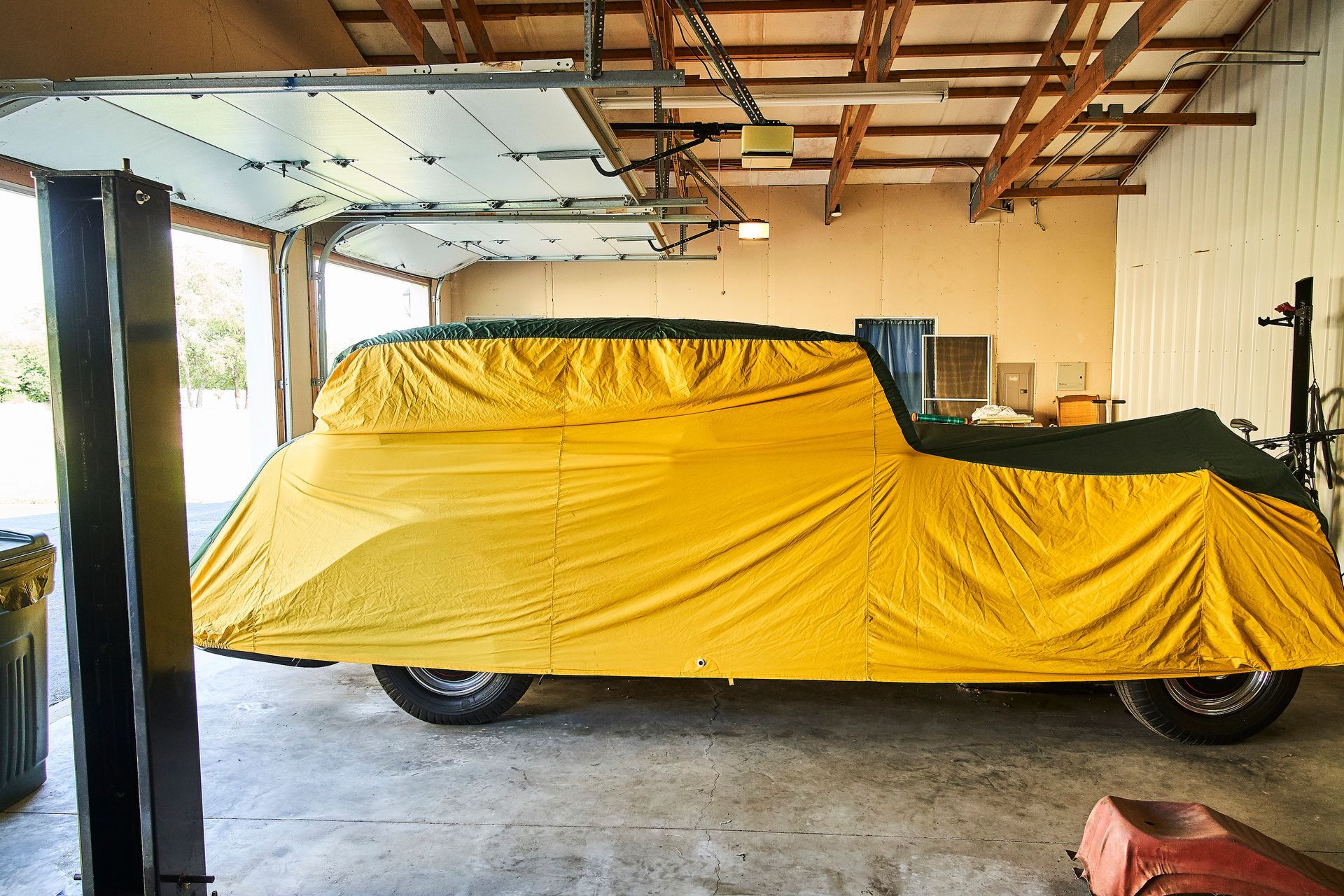 A car is covered in a yellow tarp in a garage