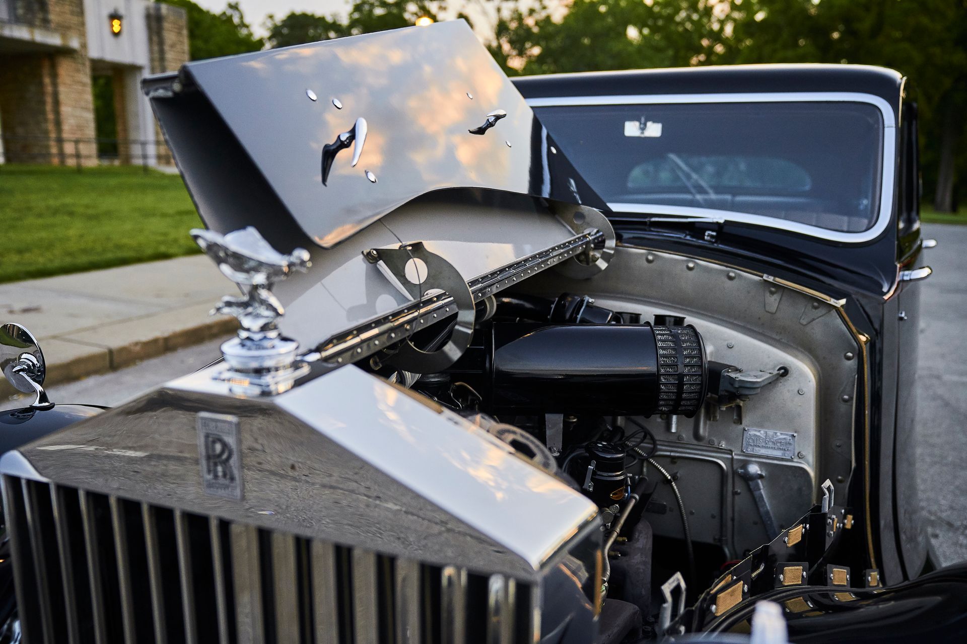 A black car with the hood open is parked on the side of the road.