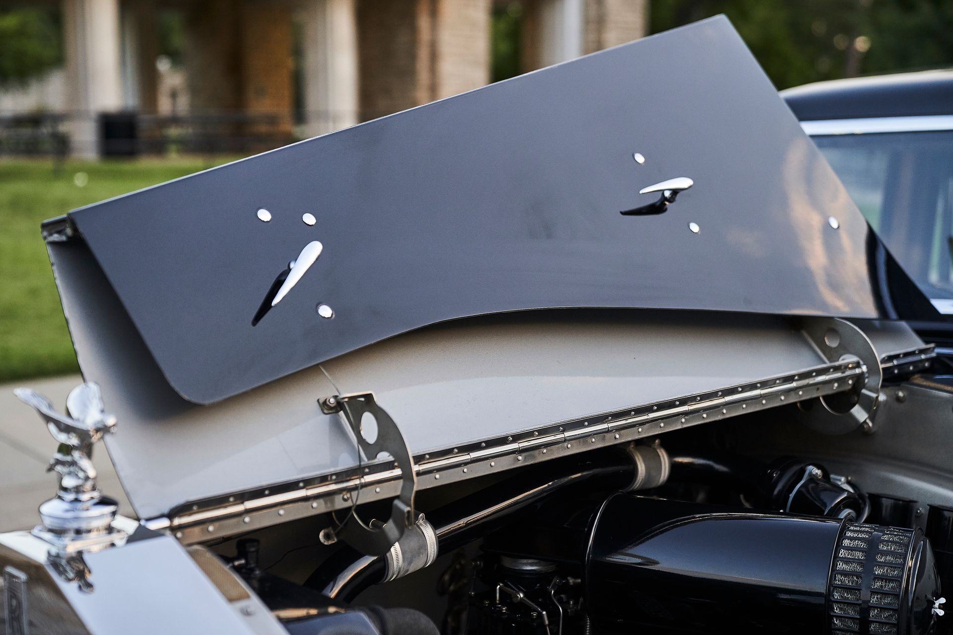A black car with the hood open and a piece of metal on the hood.