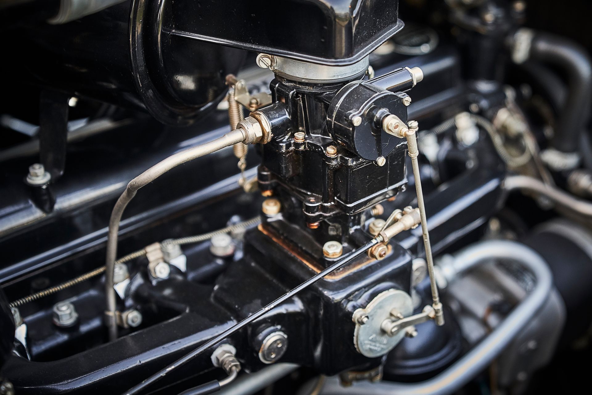A close up of a black car engine with a carburetor