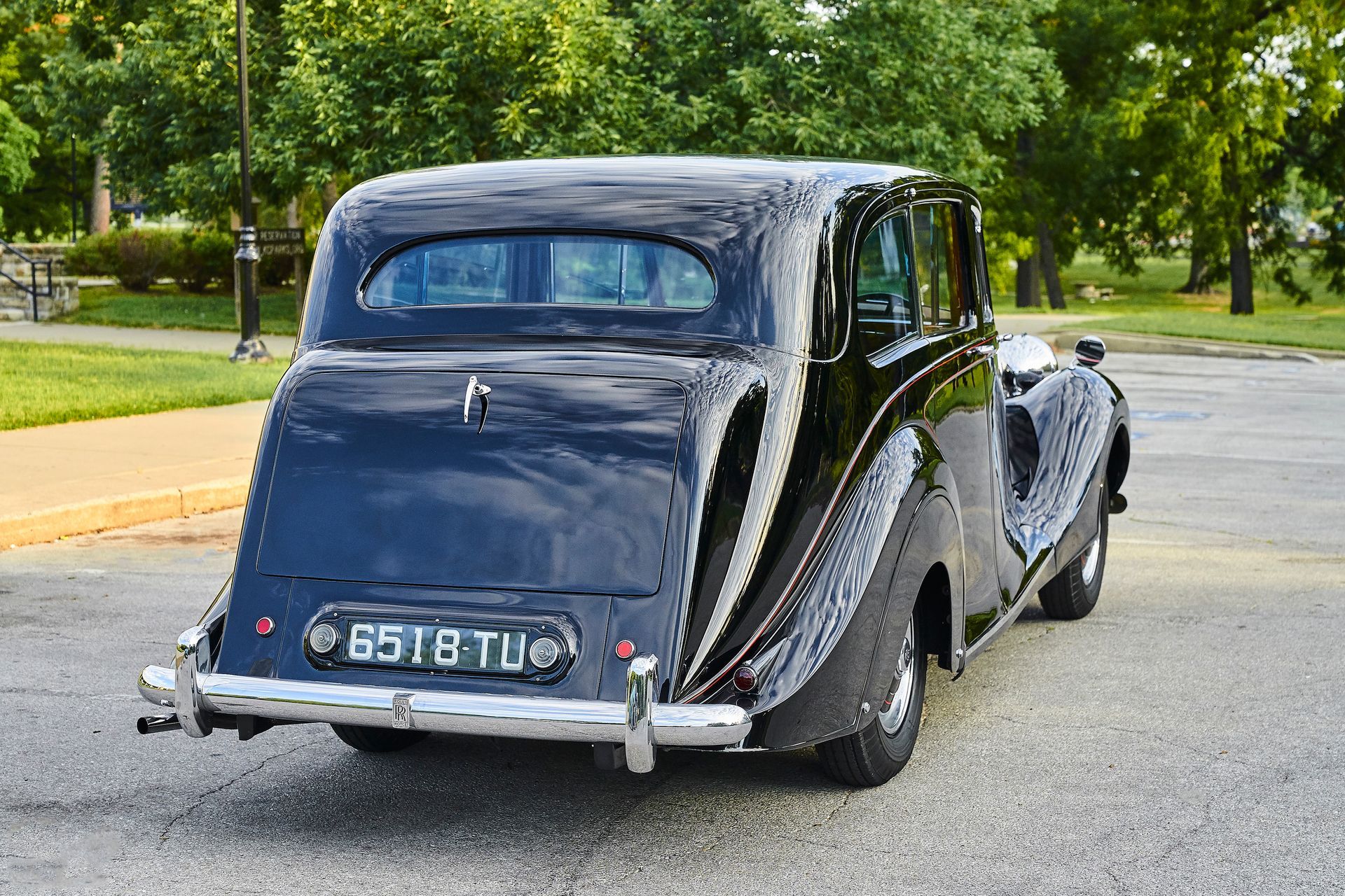 A black vintage car is parked in a parking lot in front of a park.