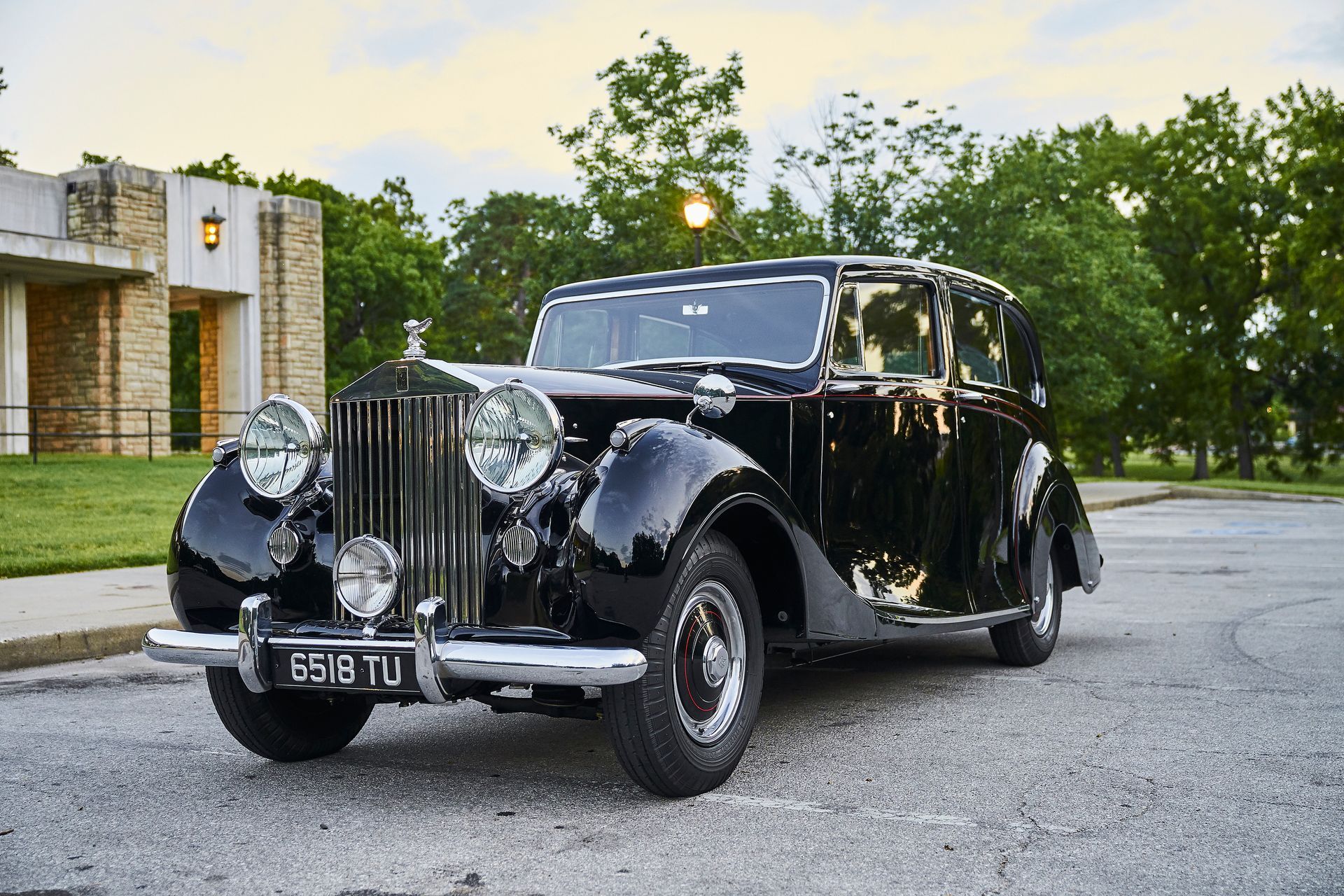 An old black rolls royce limousine is parked in a parking lot.