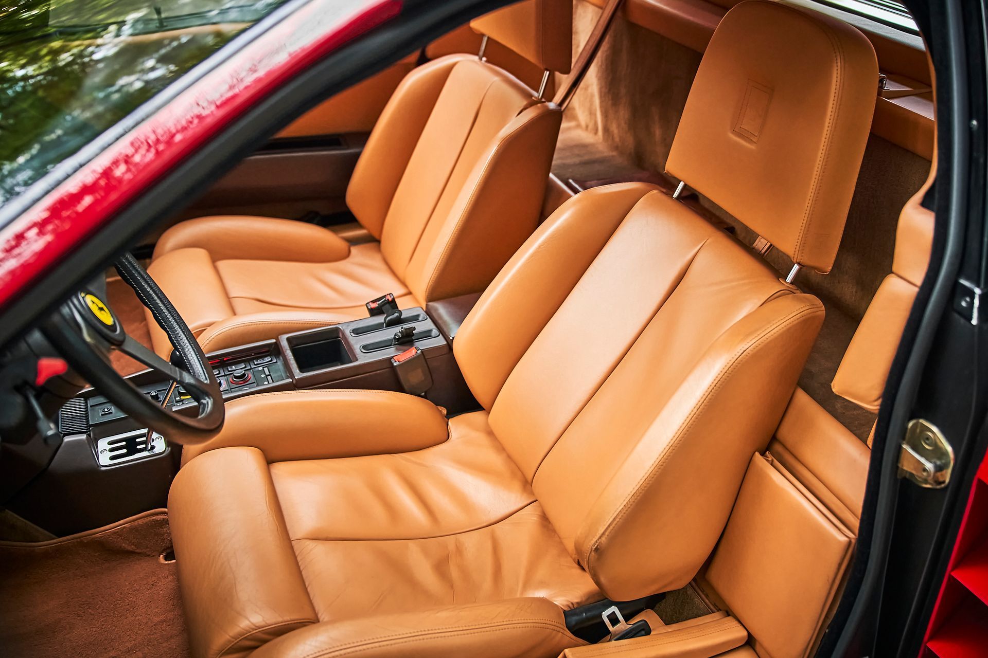 The interior of a red car with brown leather seats and a steering wheel.