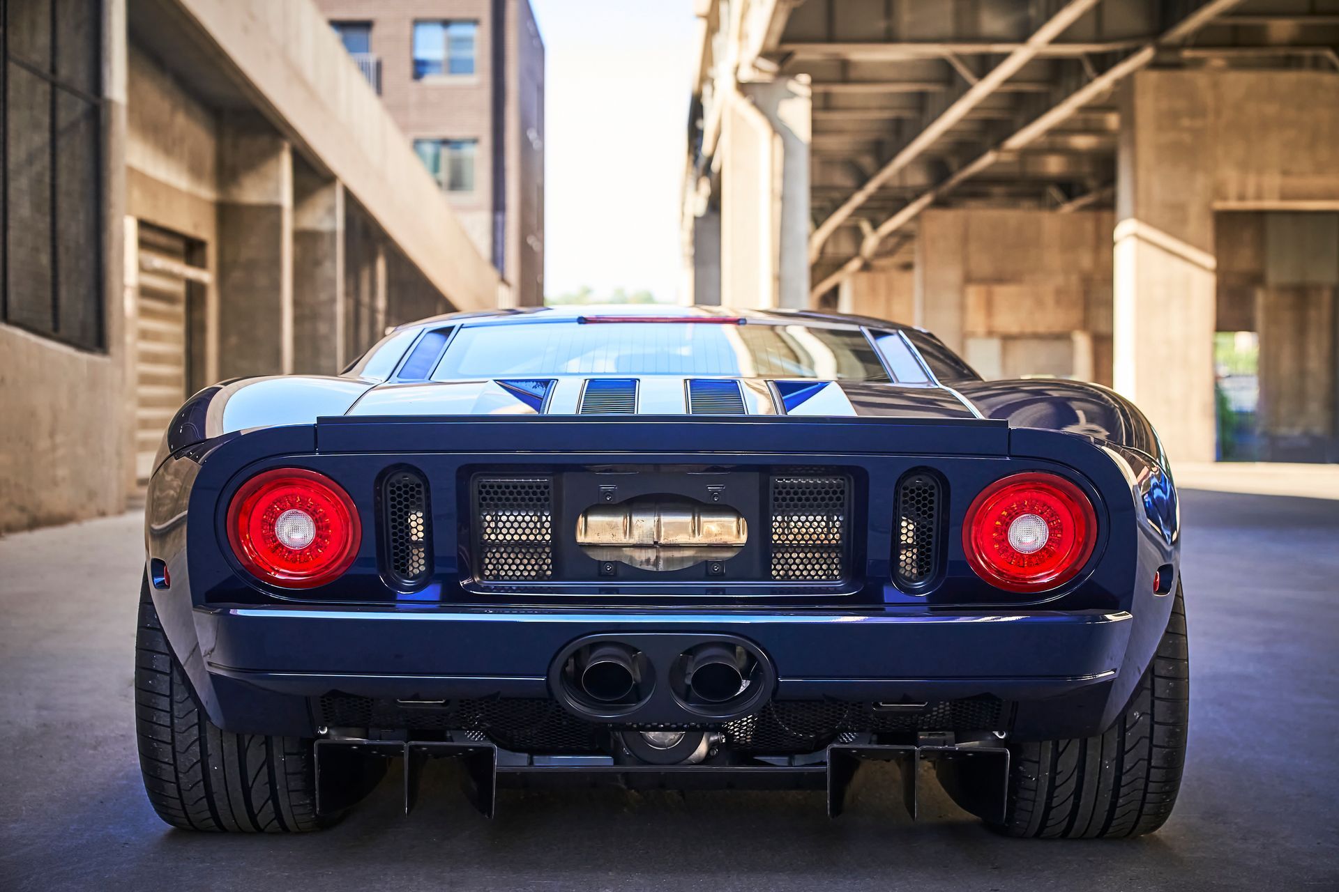 The rear end of a blue and white sports car is parked in a parking lot.