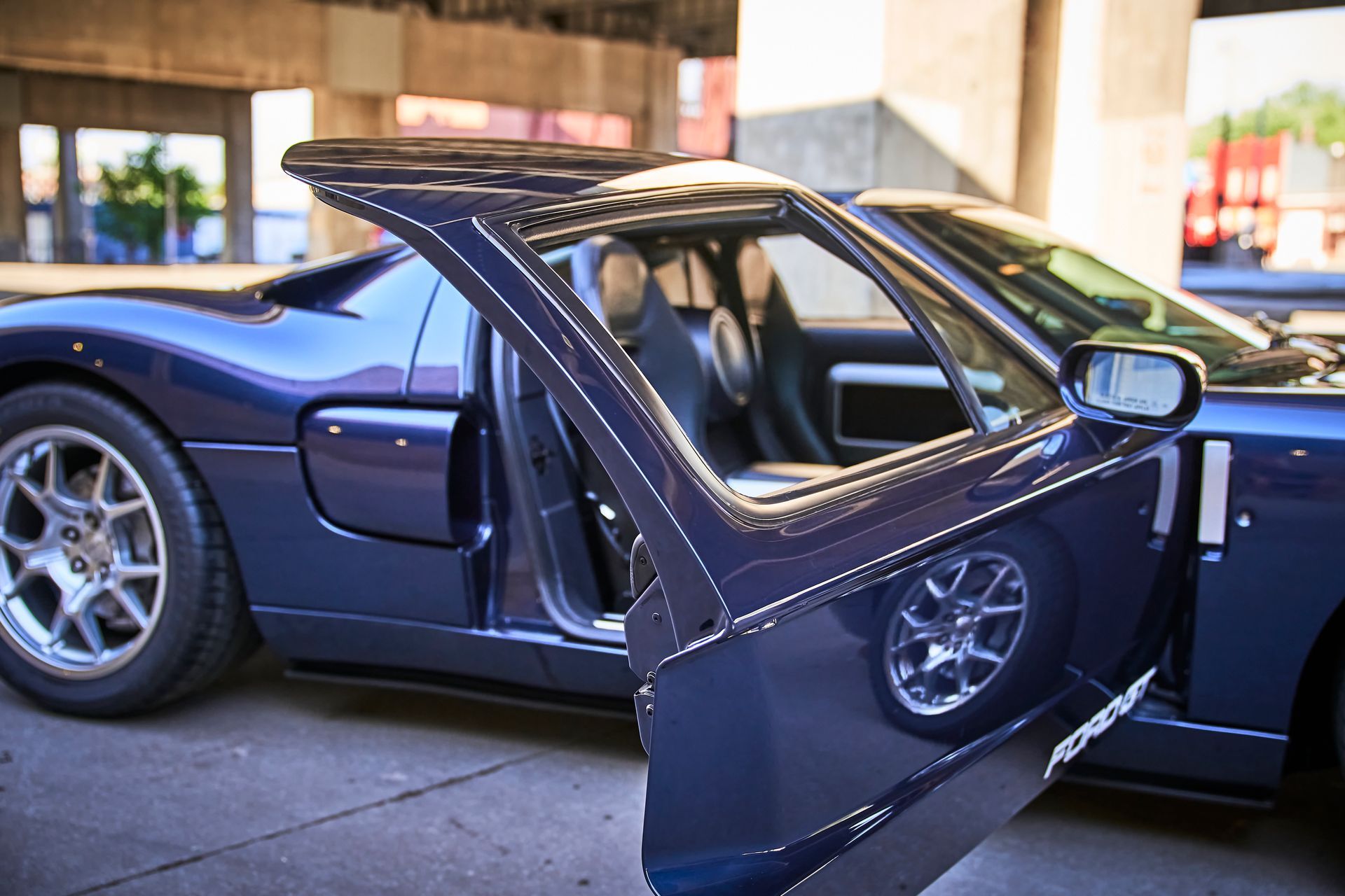 A blue sports car with the door open is parked in a parking lot.