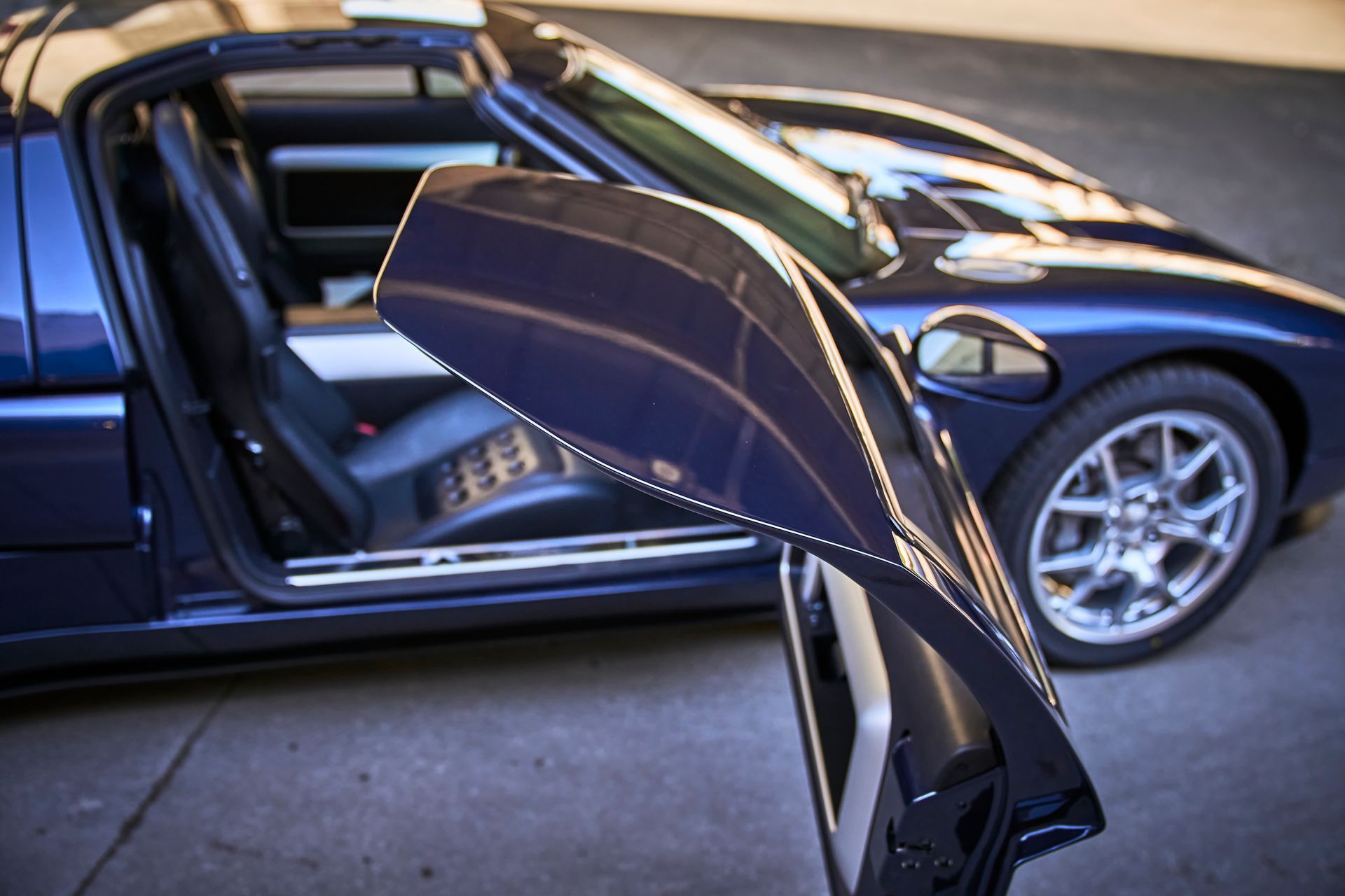 A blue sports car with the door open is parked in a parking lot.
